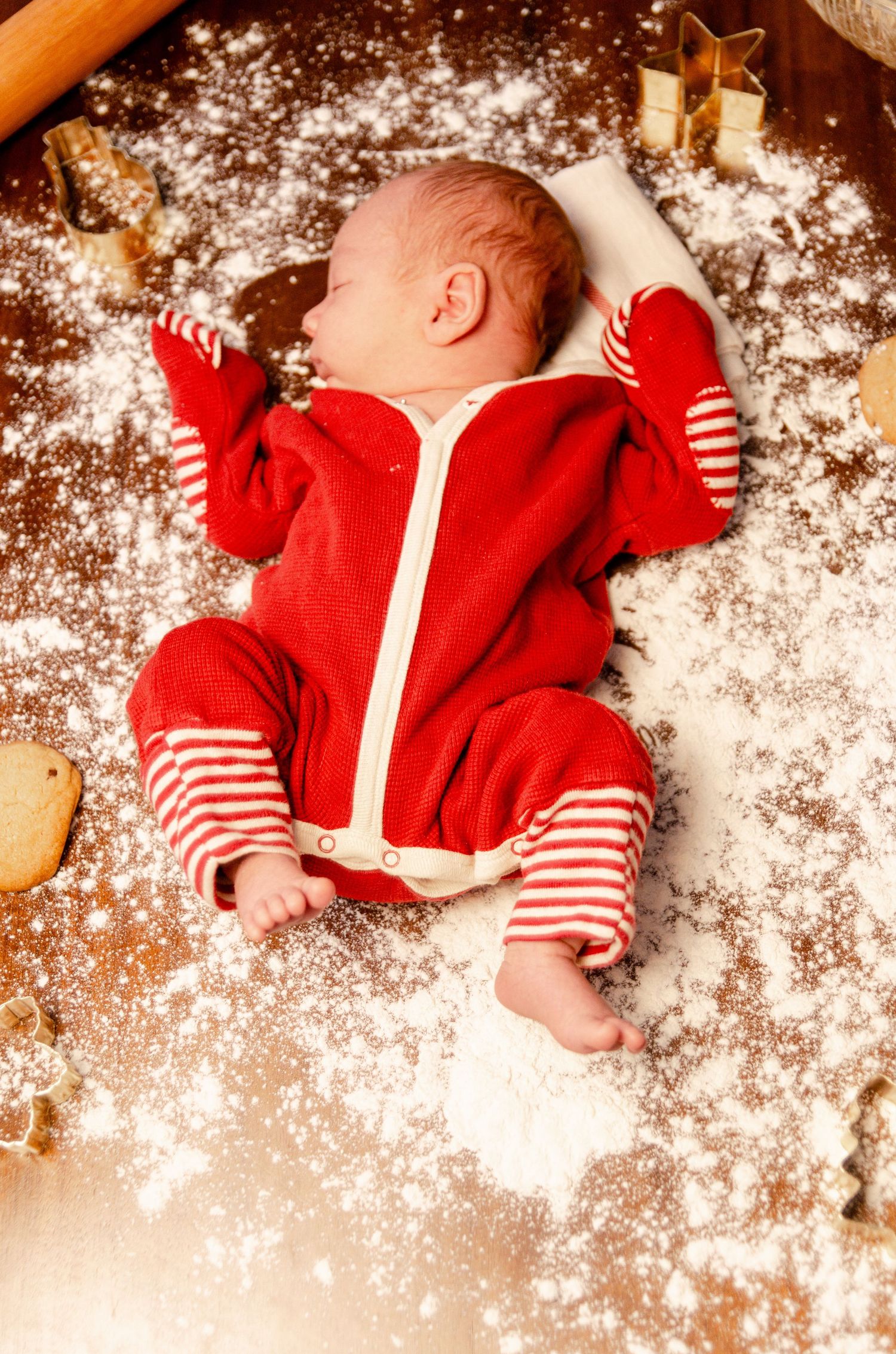 Baby in red and striped outfit lying among scattered flour on wooden surface. Newborn photography in Columbus, OH