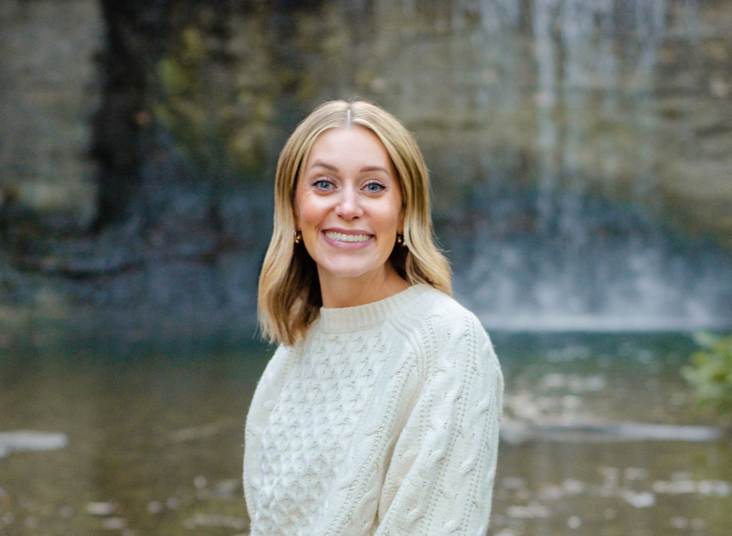 A woman in a white sweater smiles brightly by a waterfall backdrop. Headshot photos by KM Conceptions Photography in Columbus, OH.