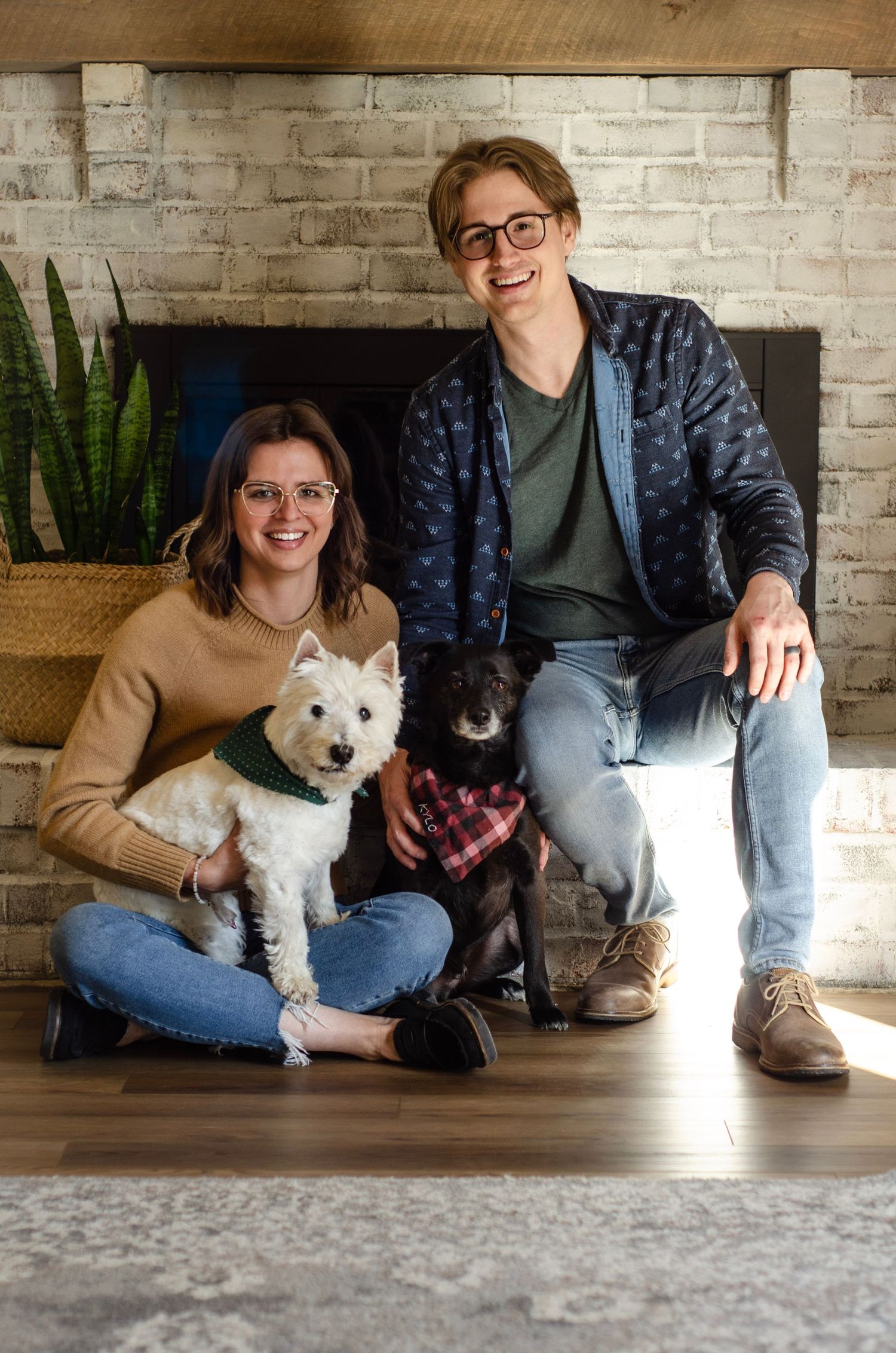 A cozy indoor scene with two dogs and their owners by a brick fireplace.