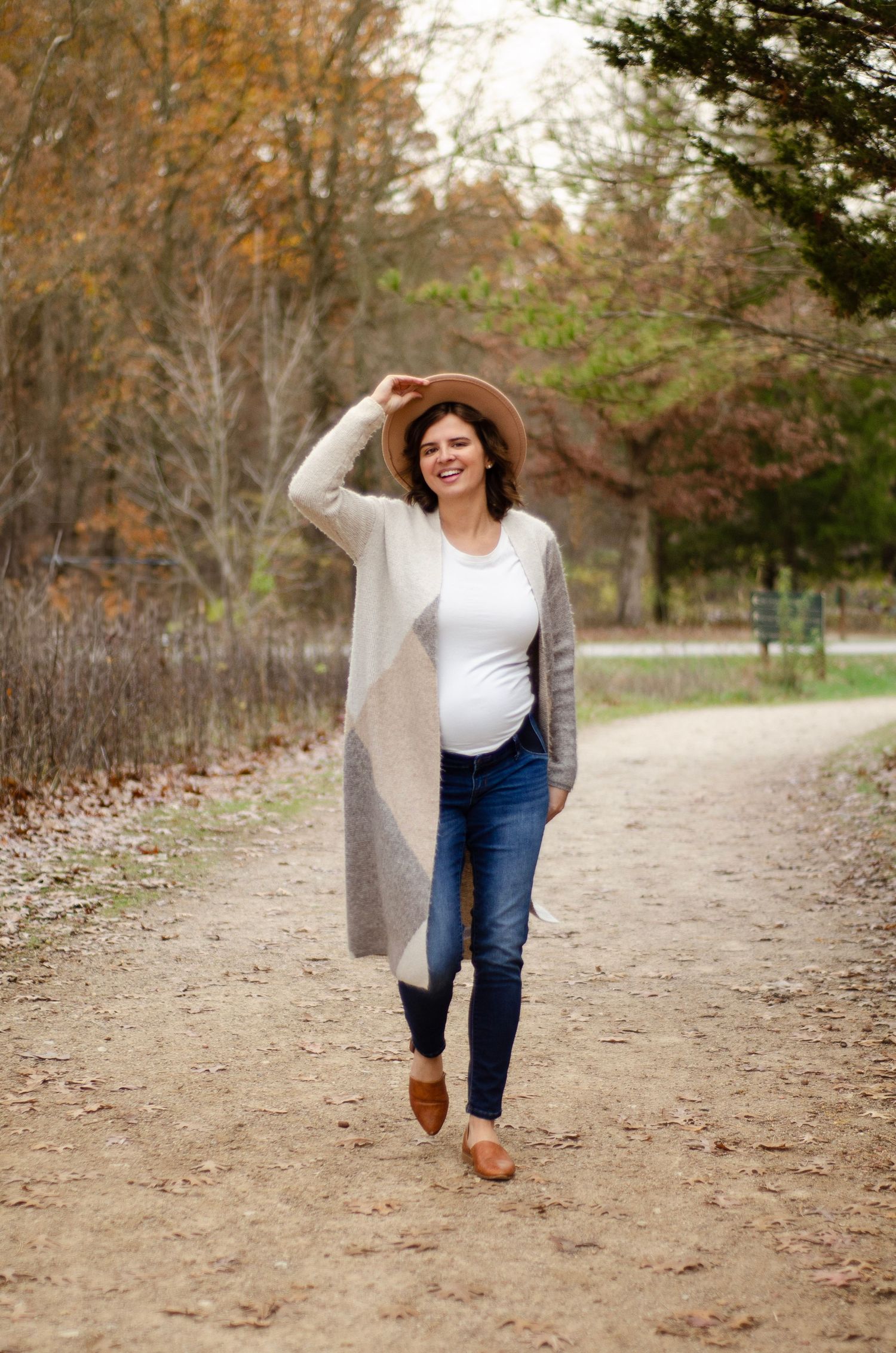 A person in jeans and gray cardigan walks along an autumn trail.