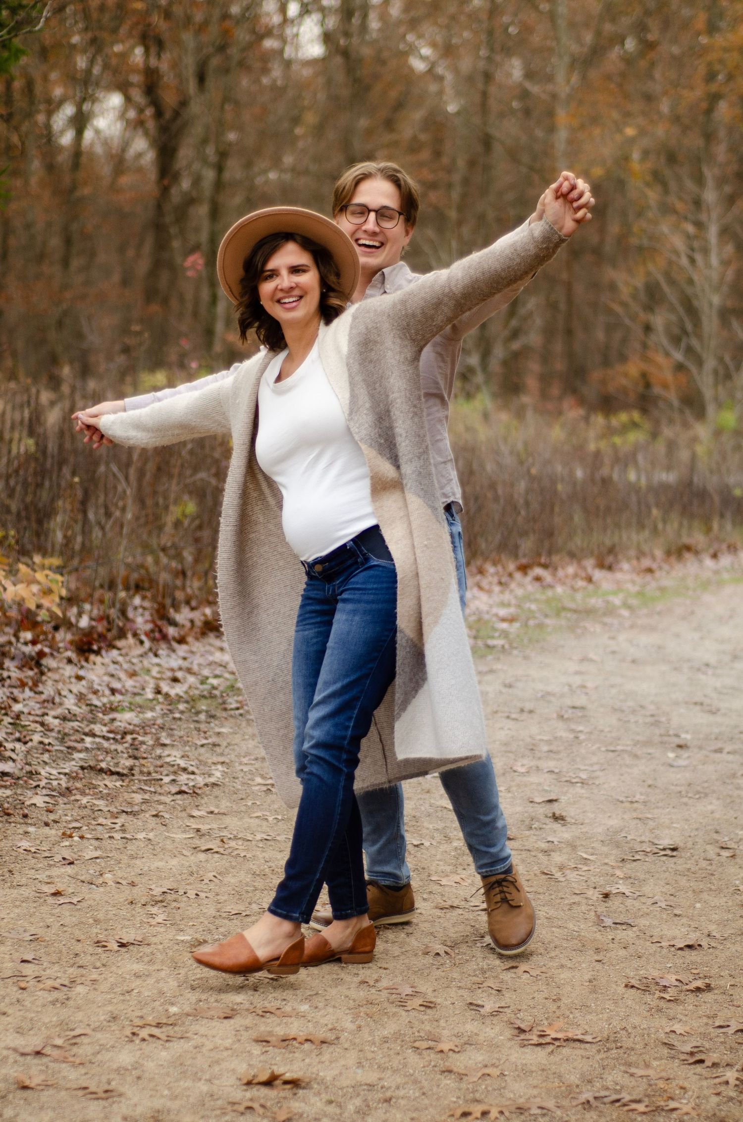 A couple playfully poses on a leaf-covered path in autumn.