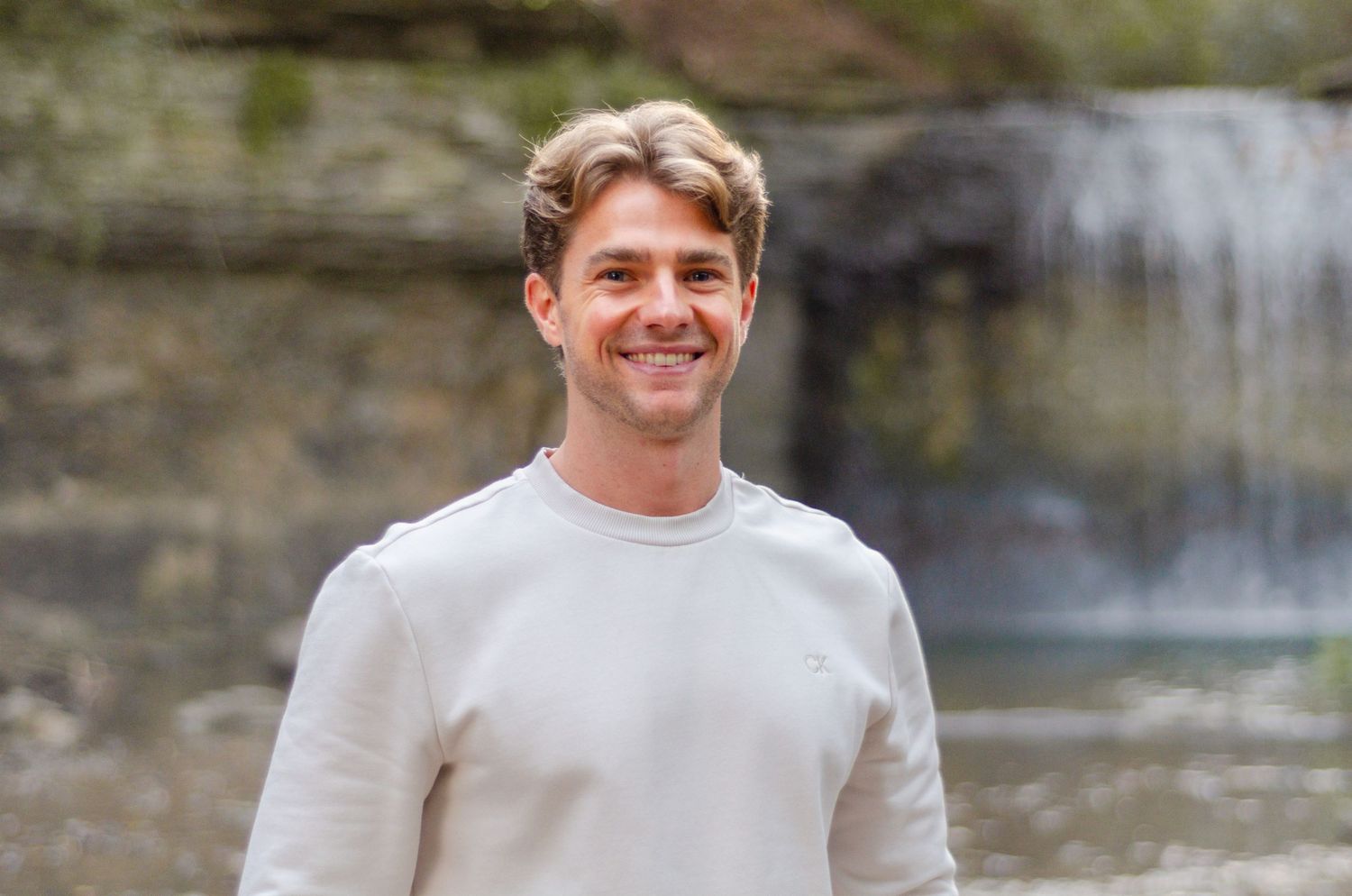 A man in a light colored sweater smiles warmly outdoors. Headshots by KM Conceptions Photography in Columbus, OH.