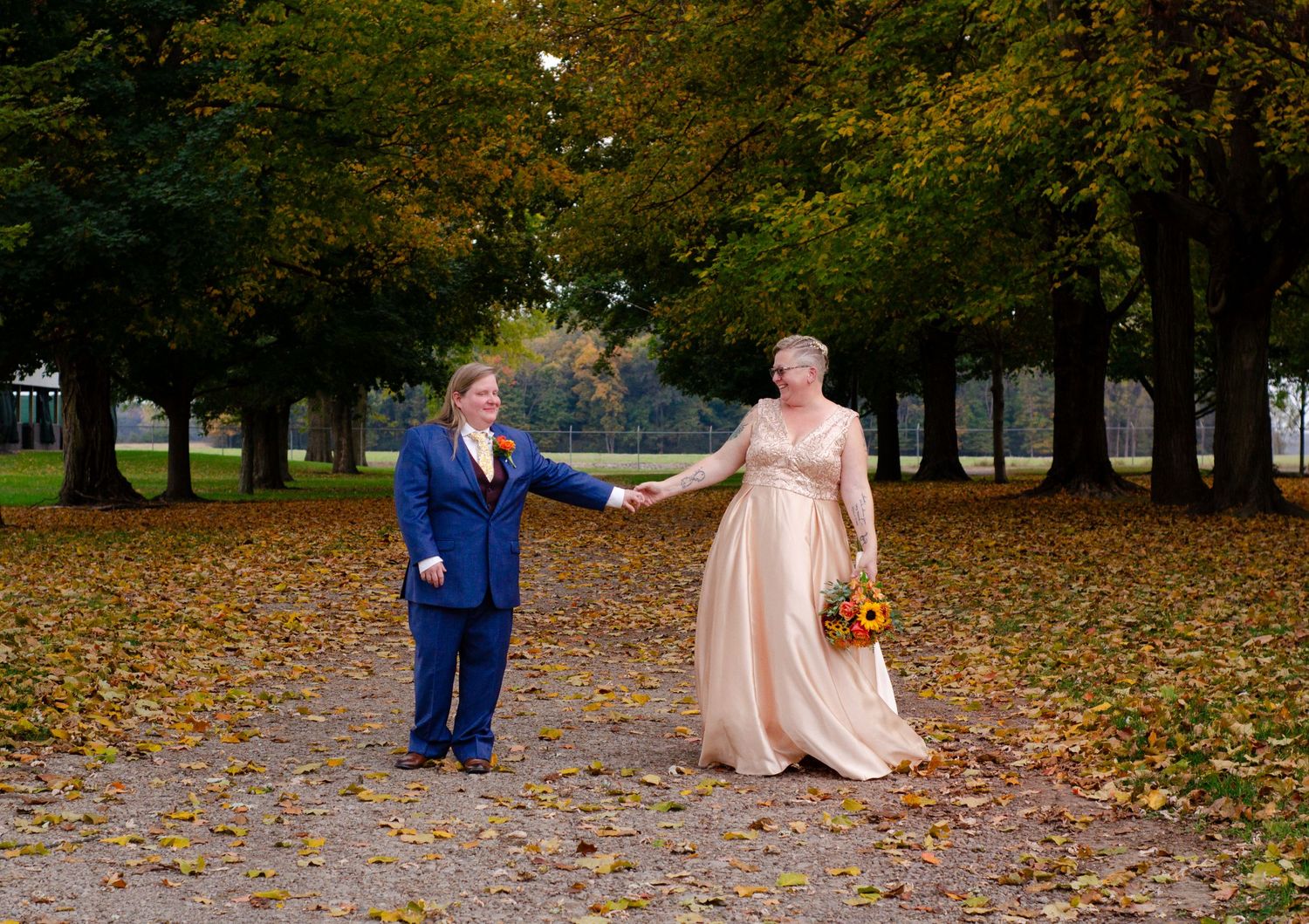 A couple walks together through a park covered in fallen autumn leaves during their wedding. Photos by KM Conceptions Photography.