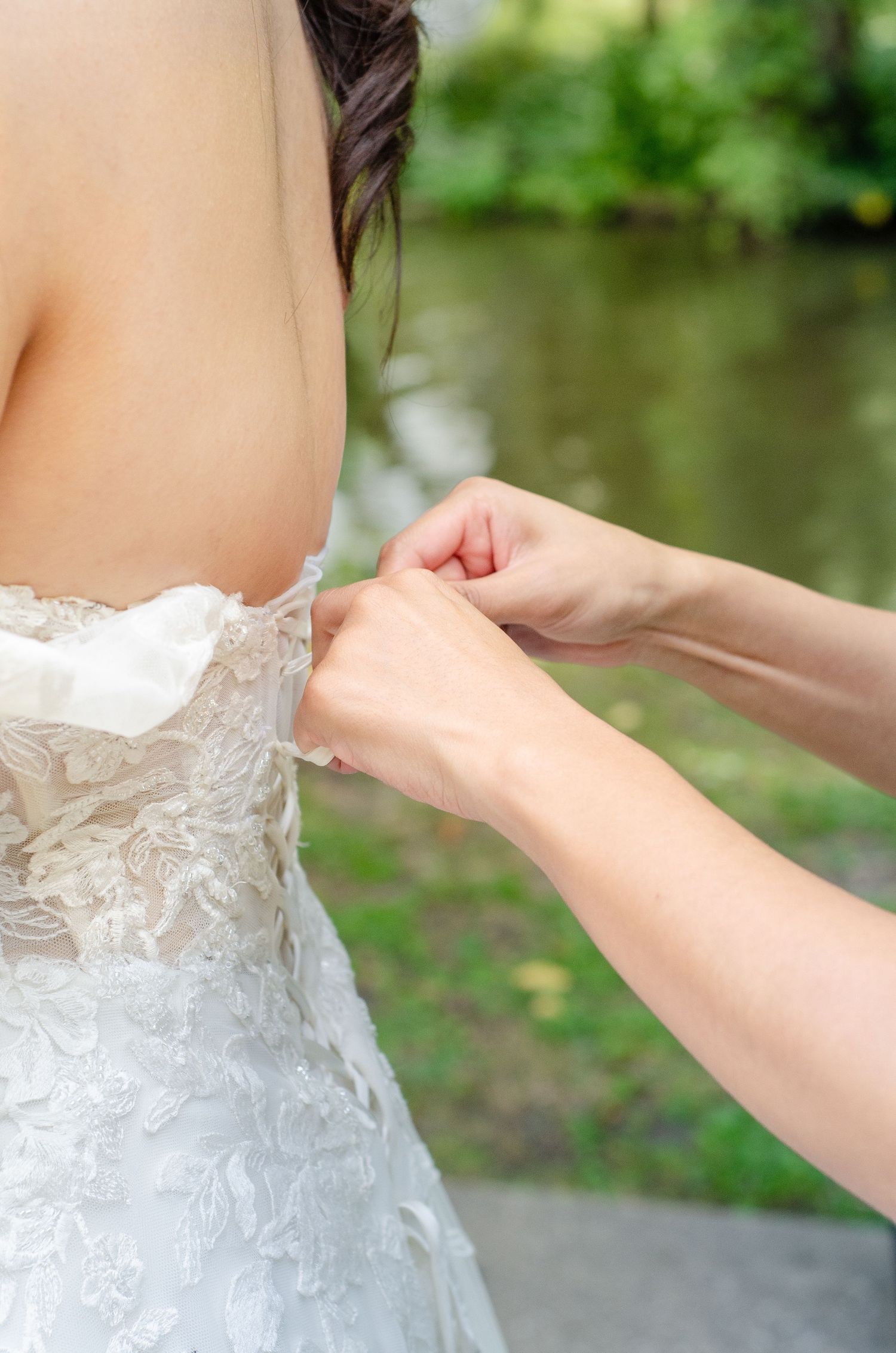 Close-up sequence showing the delicate lacing detail of a white wedding dress being adjusted against a blurred outdoor background.