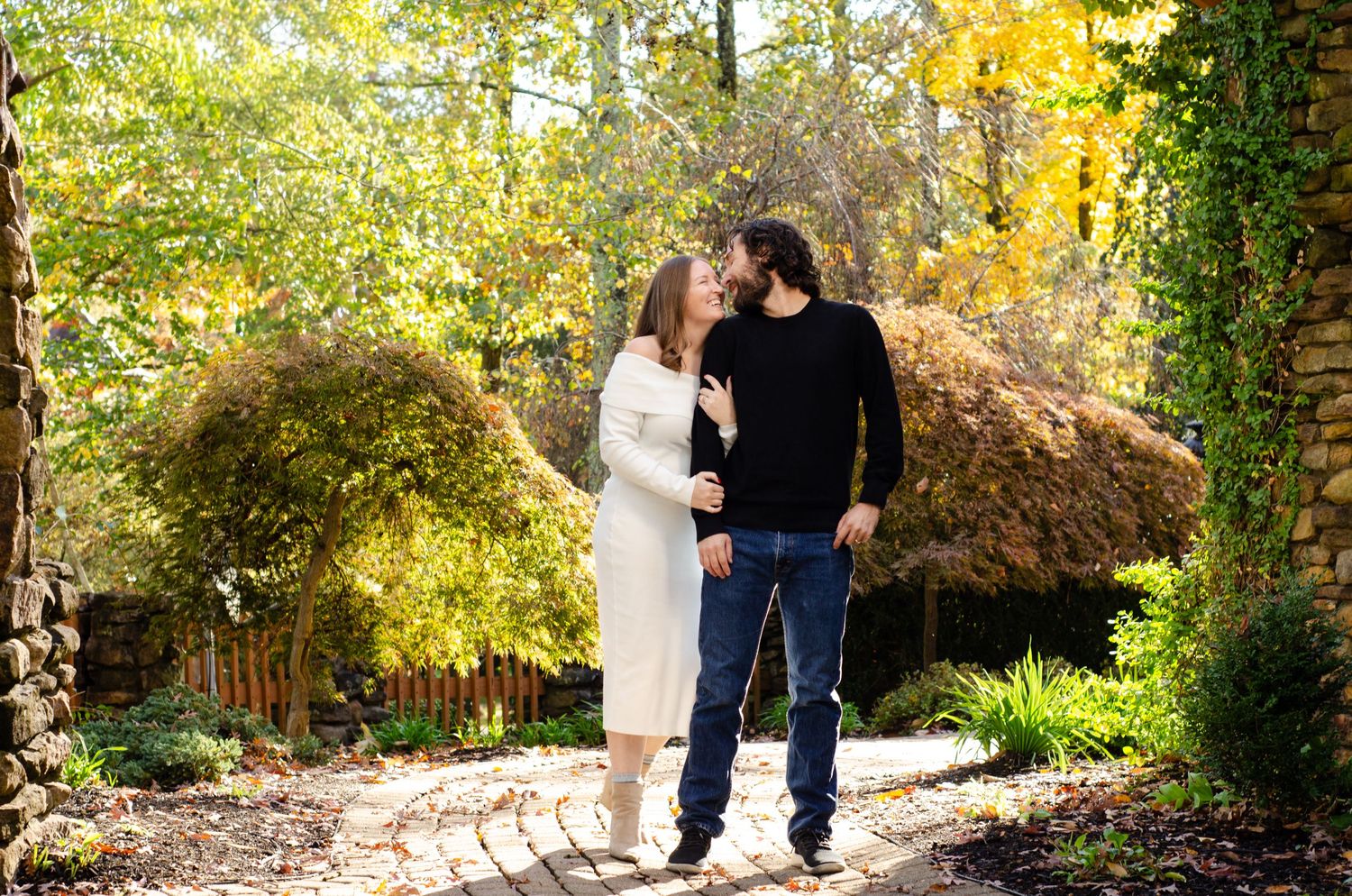 Couple sharing a kiss in an autumn garden, surrounded by colorful fall foliage and lush greenery.