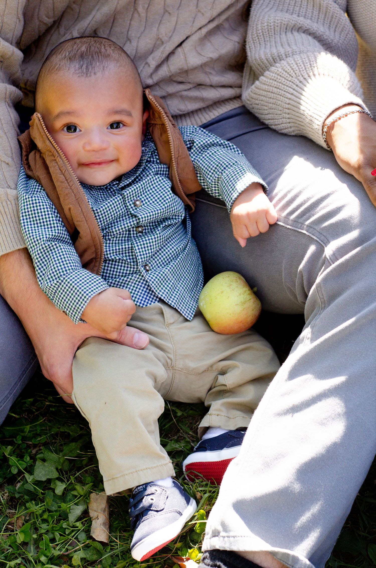 A baby in gingham and khakis sits on grass in sunlight. Family photos by KM Conceptions Photography in Columbus, OH.