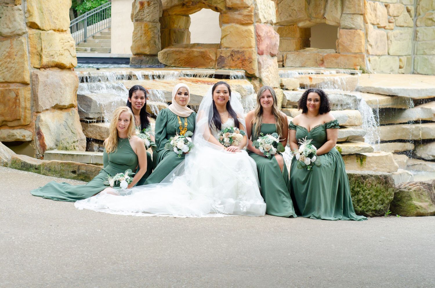 Wedding party members in sage green dresses enjoy a pool party celebration at a luxurious stone venue.