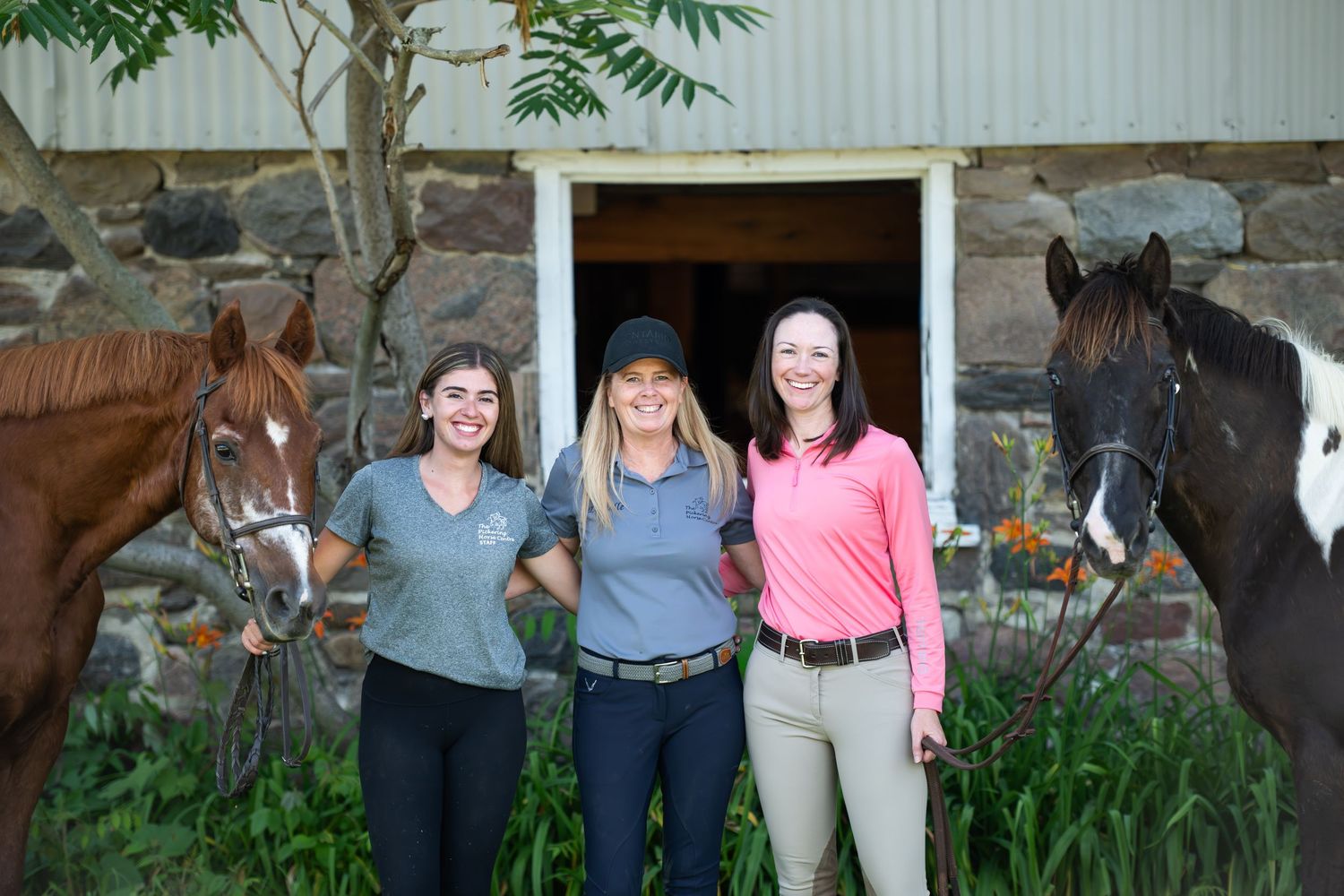 A series of people standing in a garden area with horses and trees in the background.