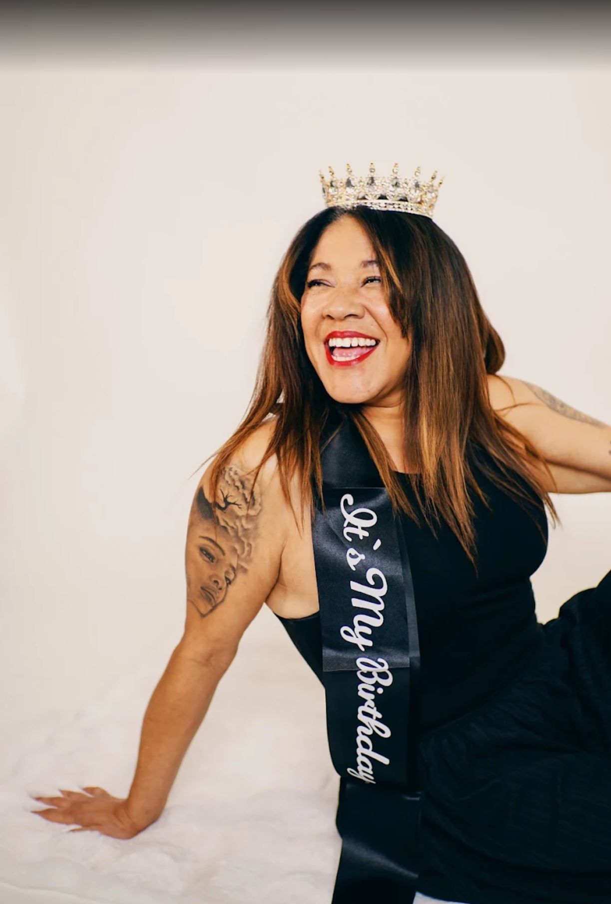 Person wearing crown and black tank top poses against white background.