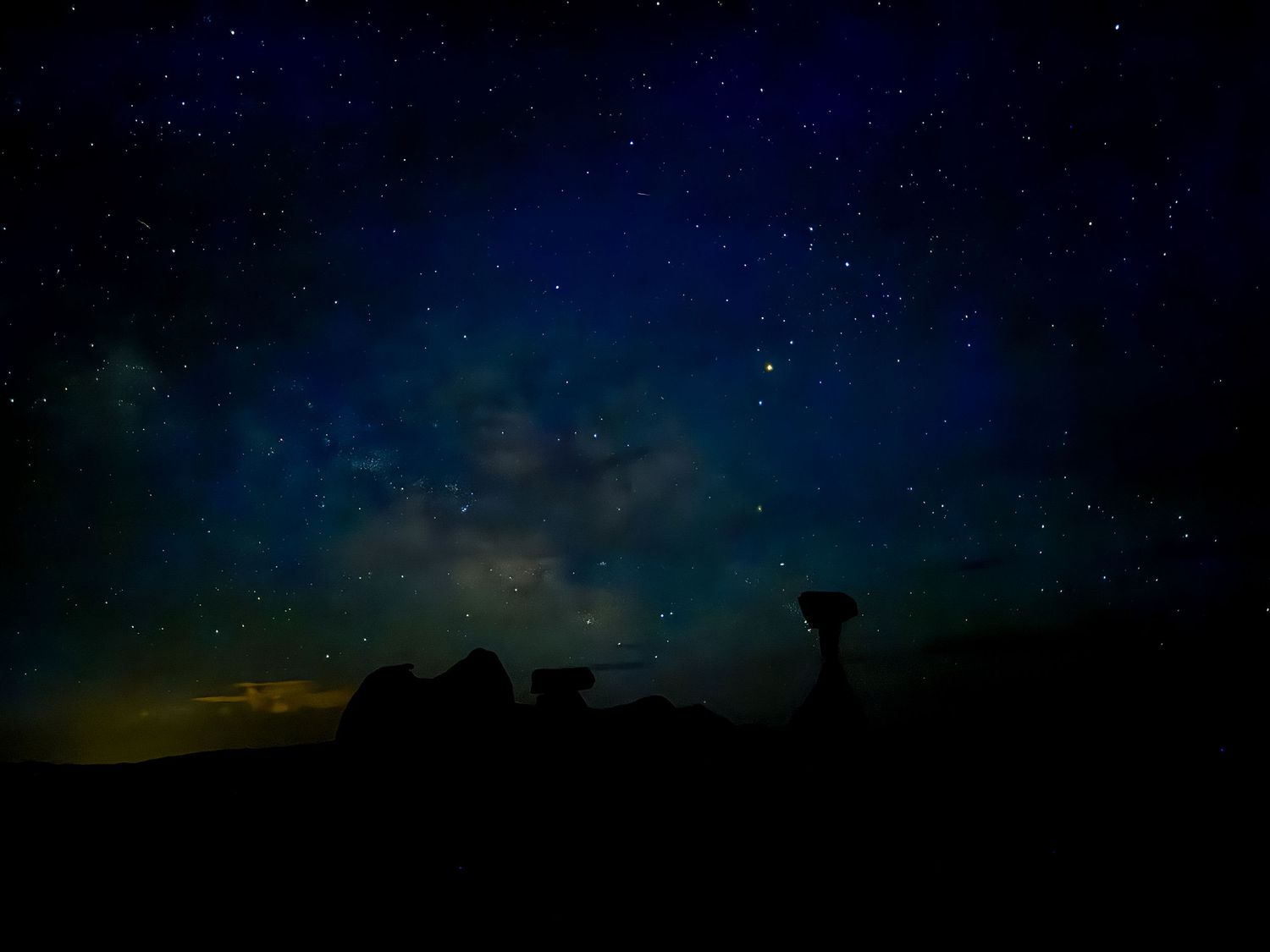 Dark silhouette of desert rock formations against a starlit night sky with hints of green aurora.