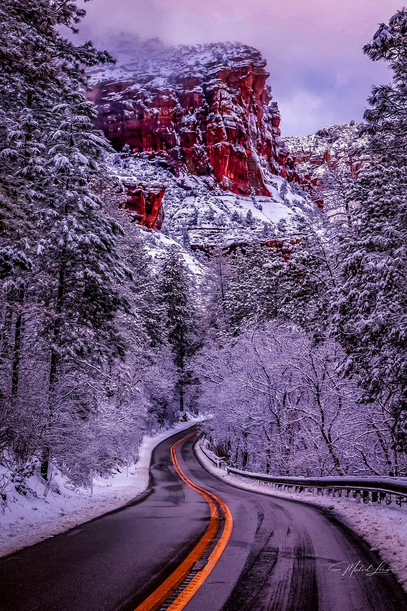 Snowy winter road winding through red rock cliffs and white-covered pine trees.