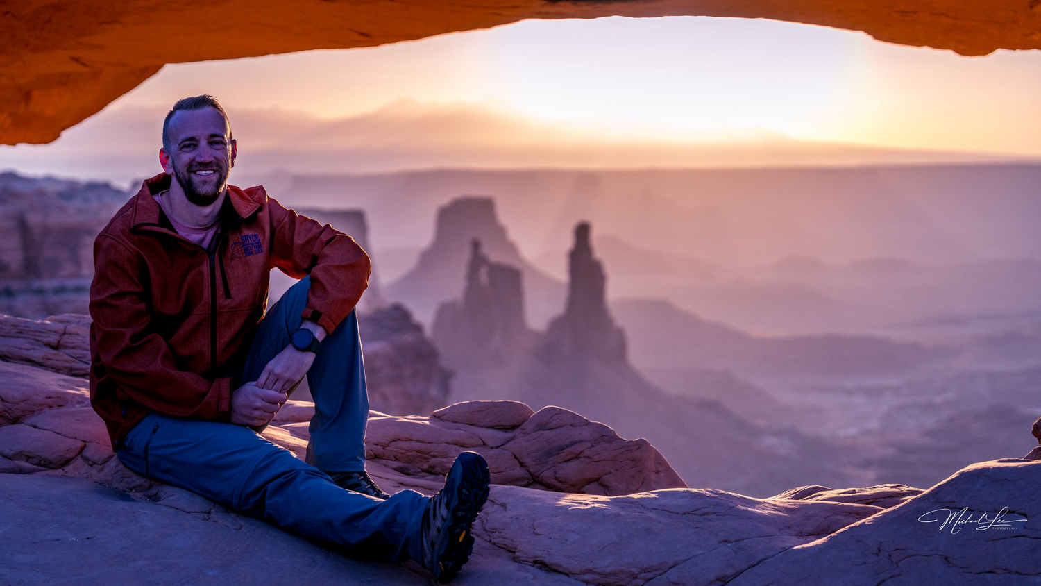 Golden sunset view through Mesa Arch with silhouetted desert rock formations in the distance.