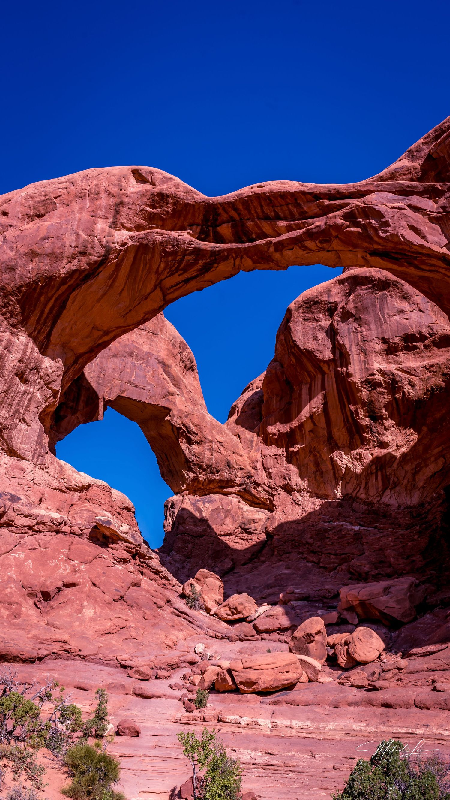 Double Arch formation in Arches National Park against bright blue sky.