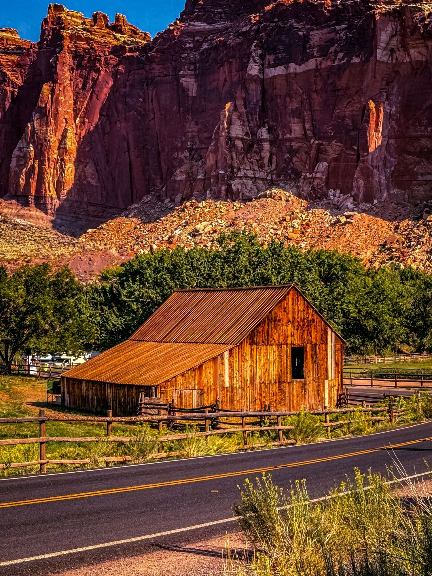 Rustic wooden barn stands against towering red rock cliffs in a desert valley landscape.