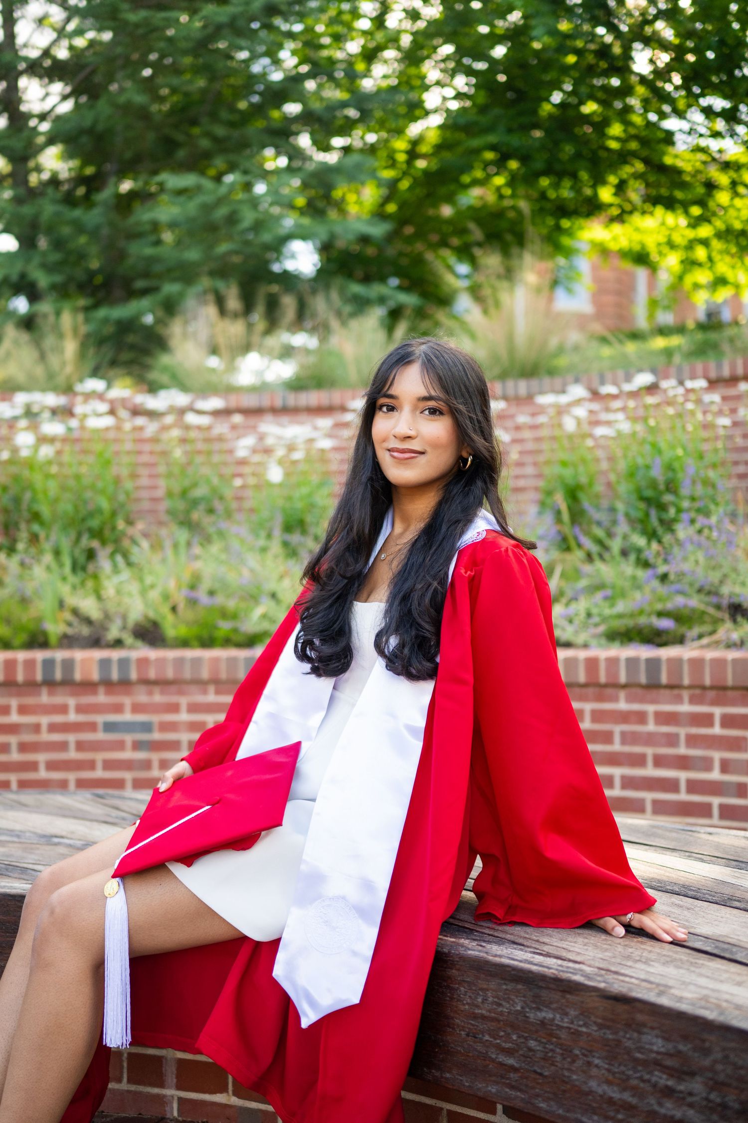 A person in a red blazer and white blouse sits on a wooden bench in a garden setting.