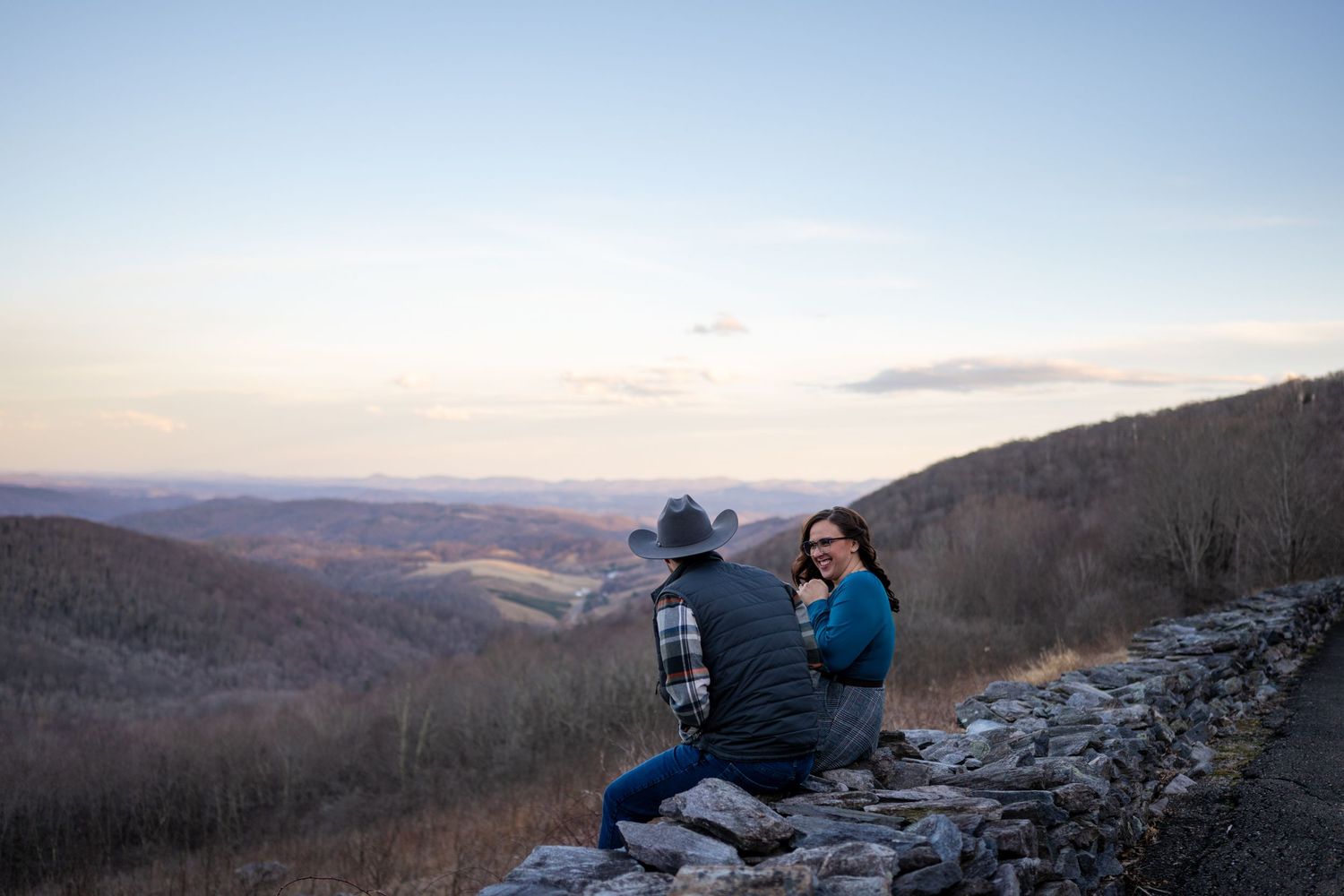 Couple sitting on a stone wall enjoying a scenic mountain valley sunset view.