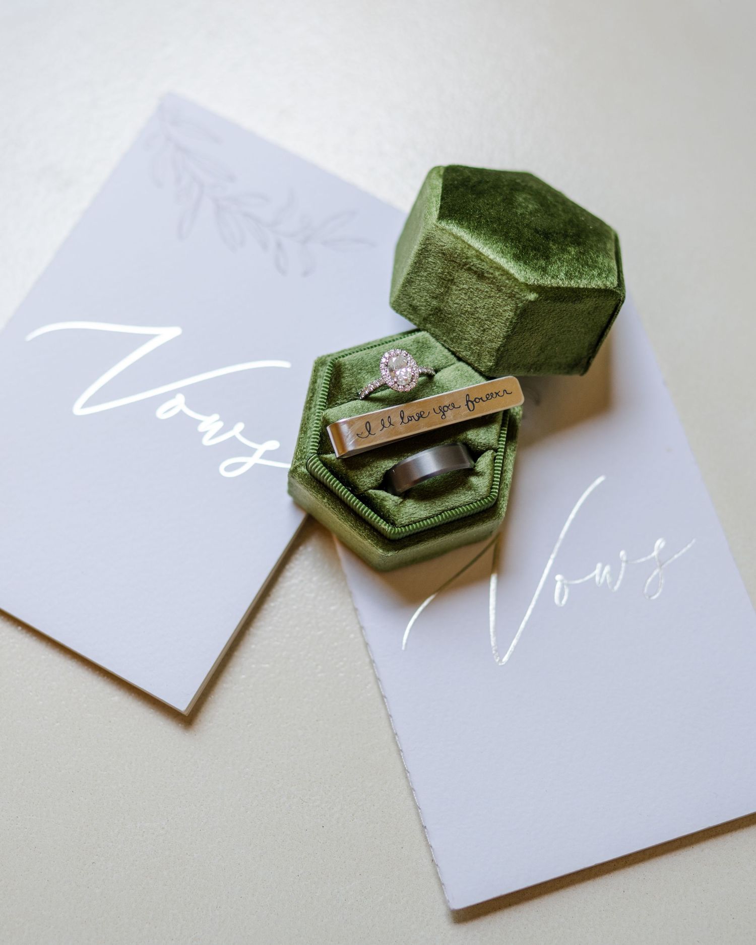 A green velvet ring box with a diamond engagement ring sits between two white cards on a light surface.