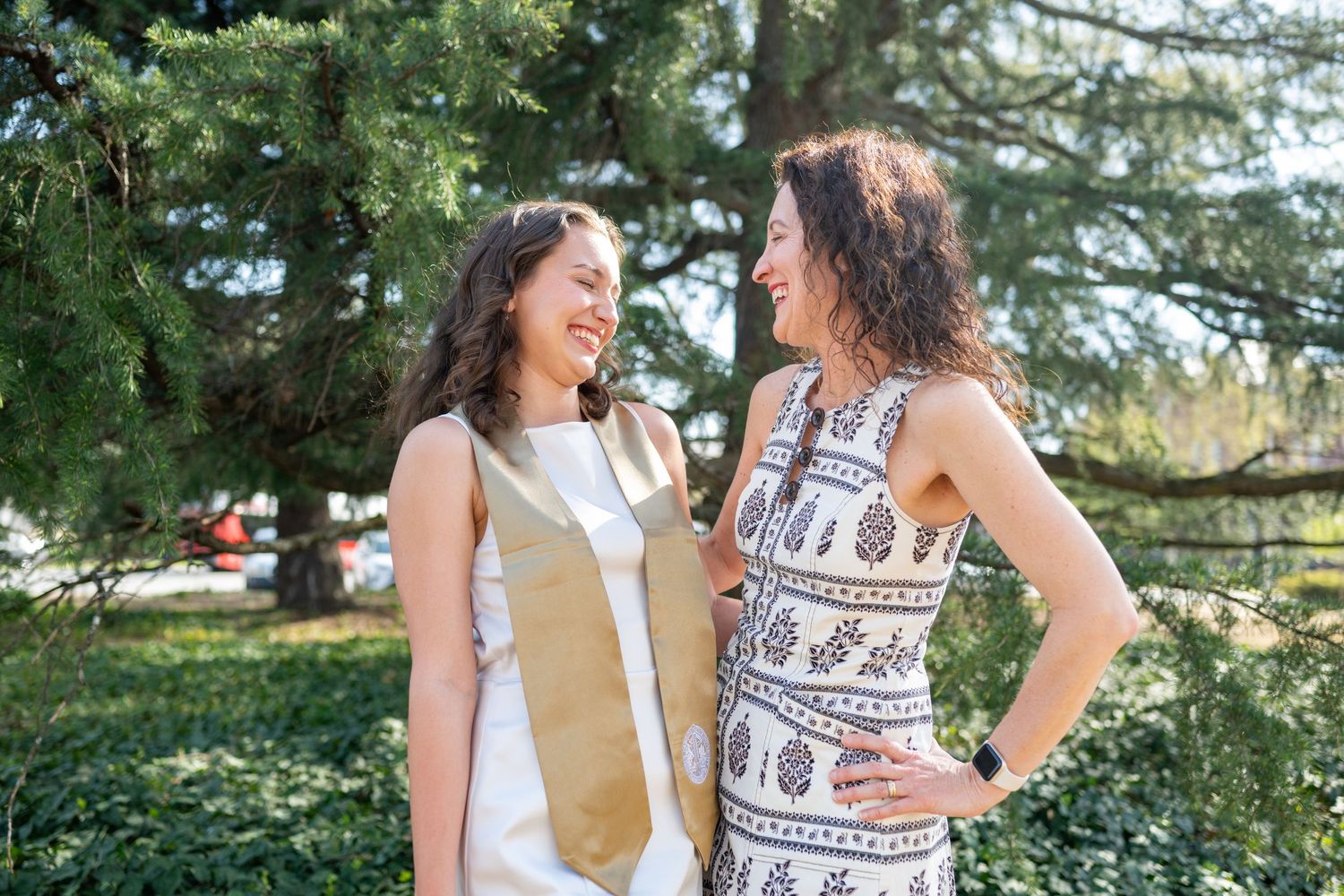Two people in summer outfits laughing and enjoying a sunny day outdoors in a natural setting.