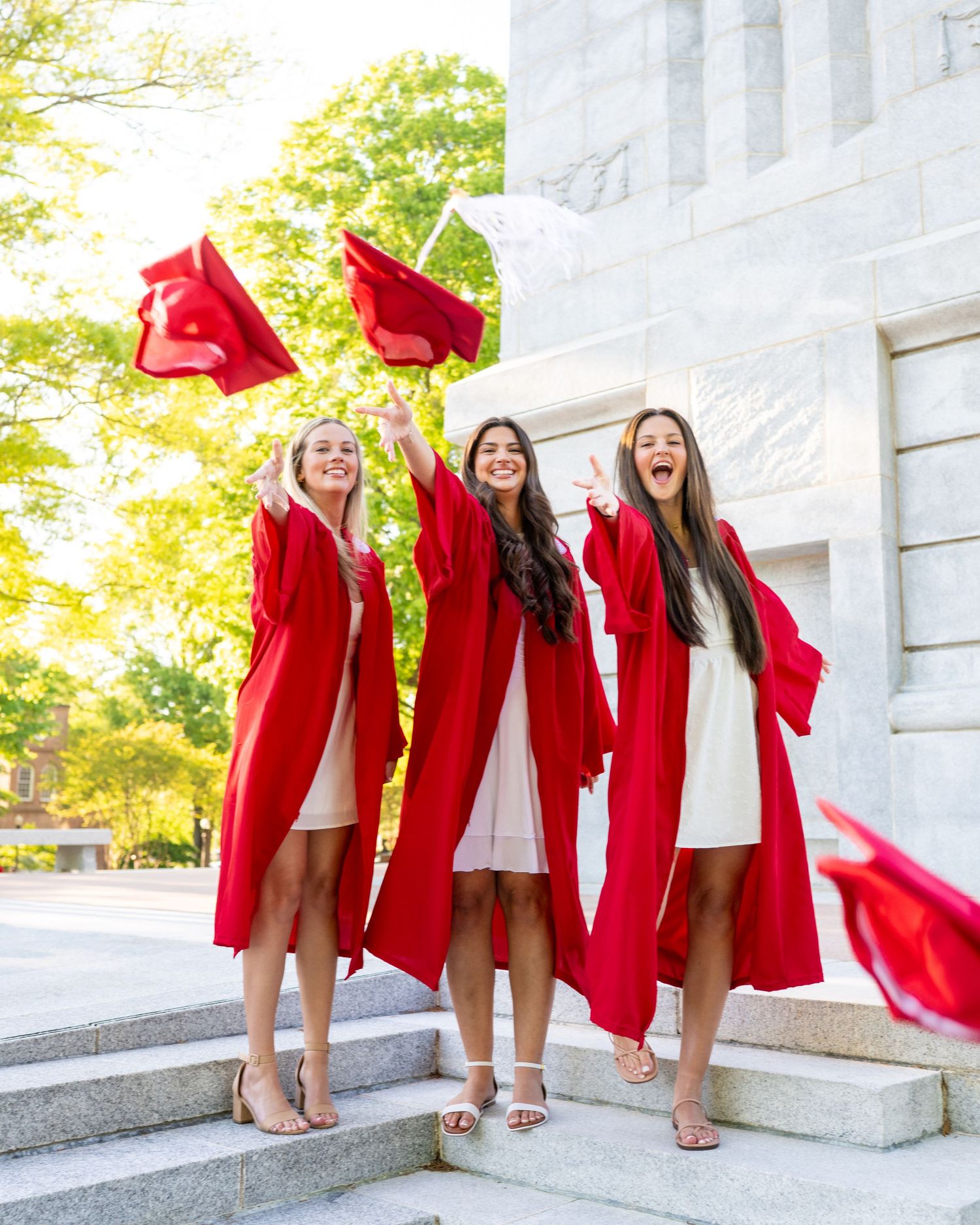 A group in red graduation gowns pose playfully on stone steps during a celebratory photoshoot.