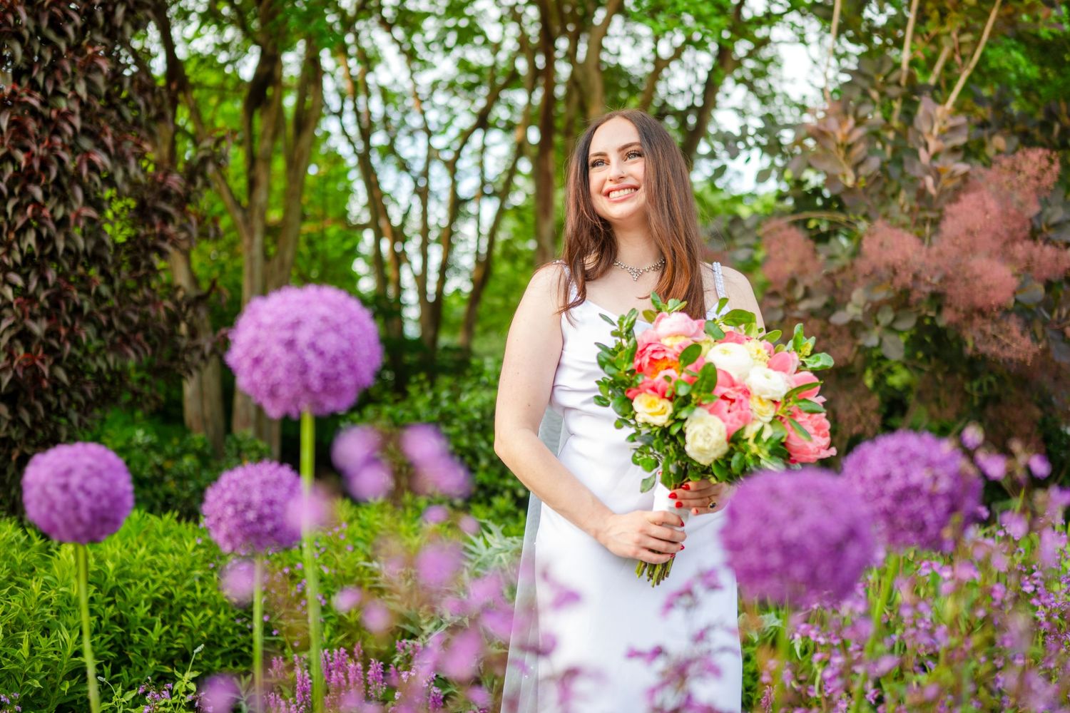 A wedding photoshoot in a blooming garden with purple allium flowers and pink cherry blossoms creating a romantic backdrop.