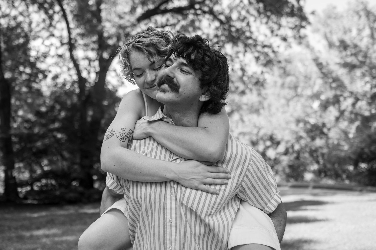 Black and white photo showing a joyful piggyback ride in a sunlit park with striped clothing.