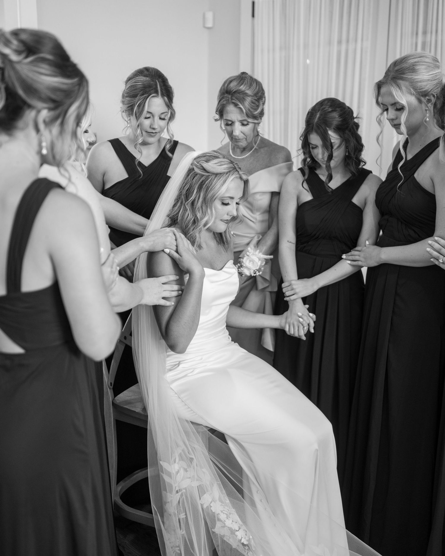 A bride in a white gown and bridesmaids in black dresses share candid moments during pre-wedding preparations.