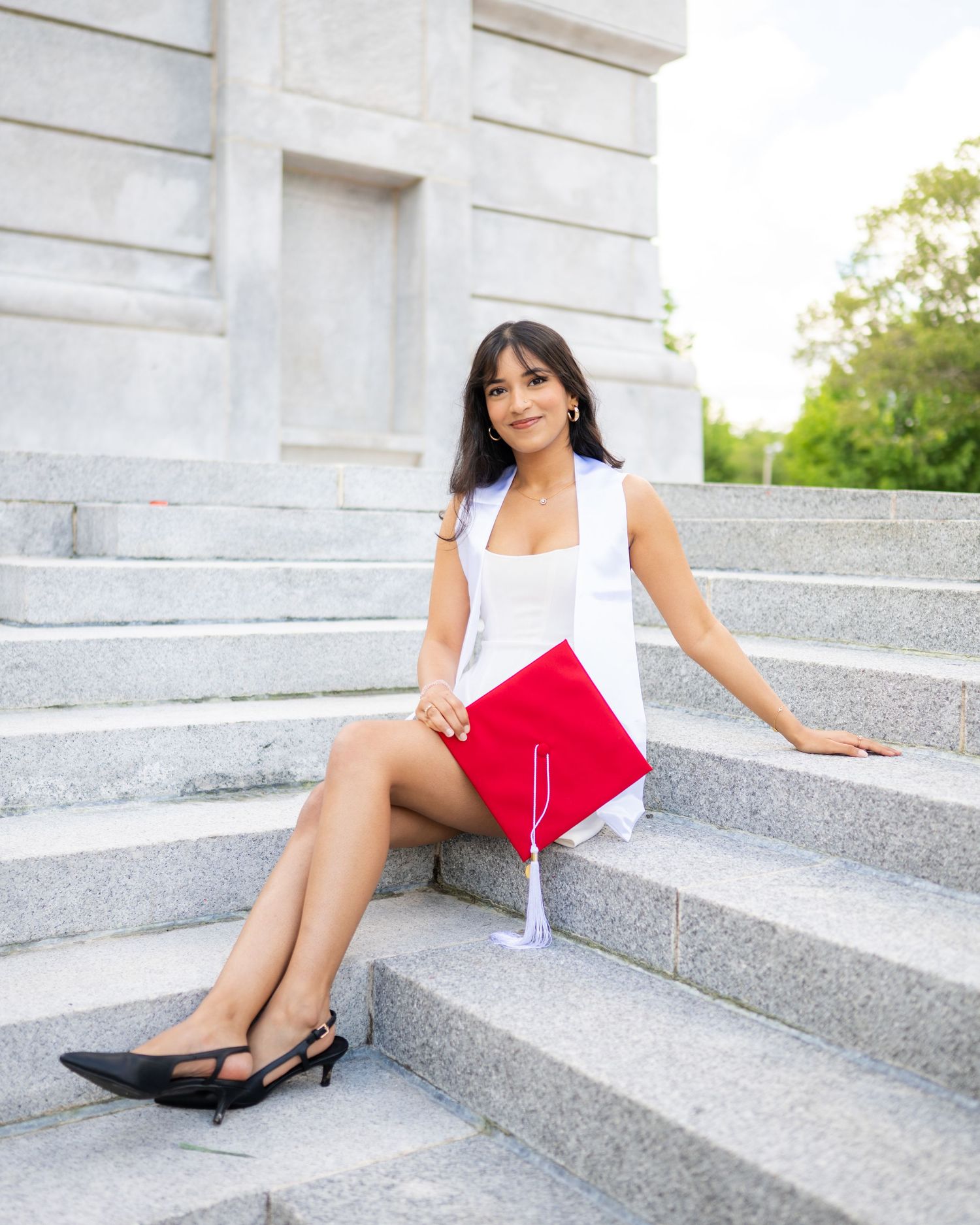 A woman in business attire sits gracefully on white marble steps while holding a red folder.