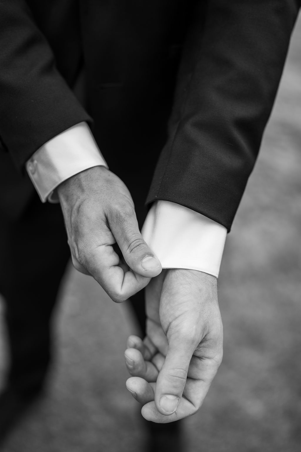 Close-up black and white photo of groom adjusting cufflinks on wedding day.