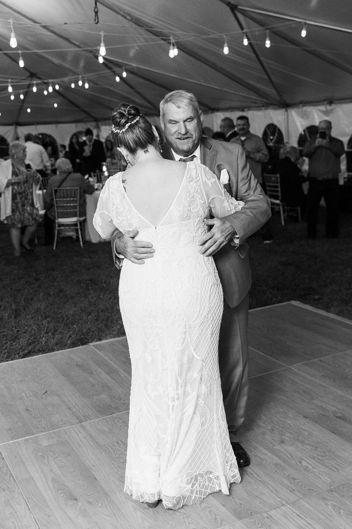 Bride and father share an emotional first dance under string lights at elegant tented wedding reception.