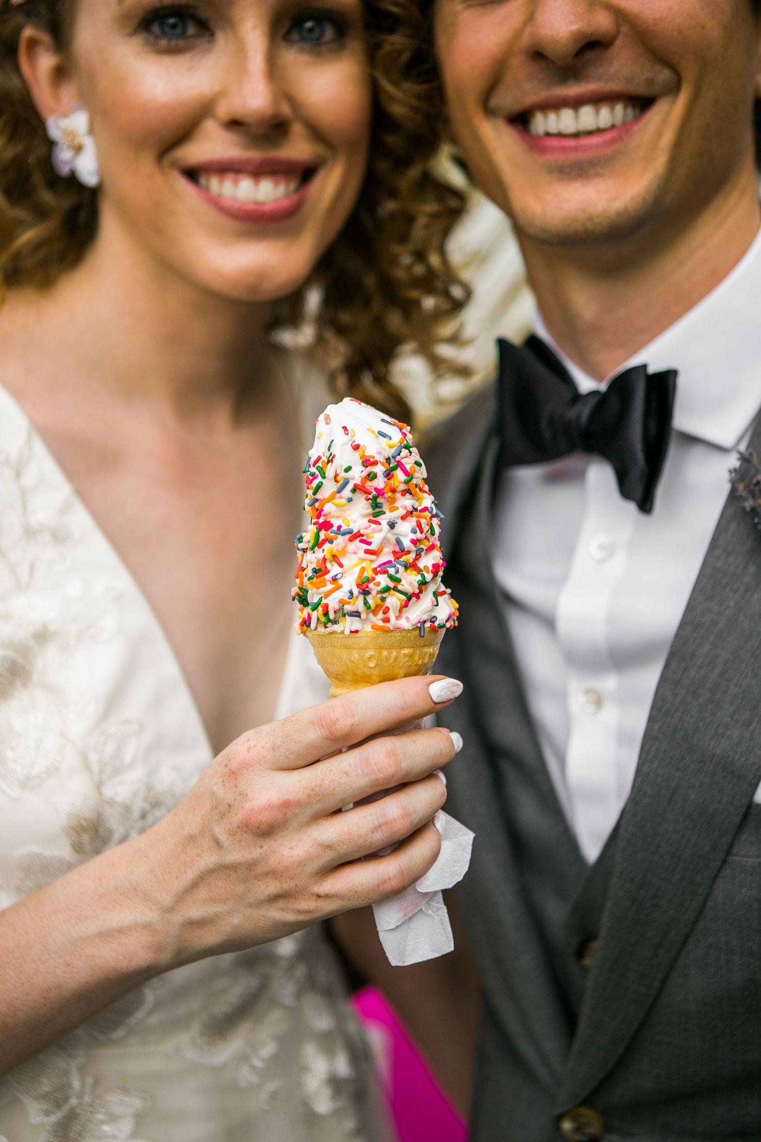 Bride and groom smiling while holding a colorful sprinkle soft serve ice cream cone together.