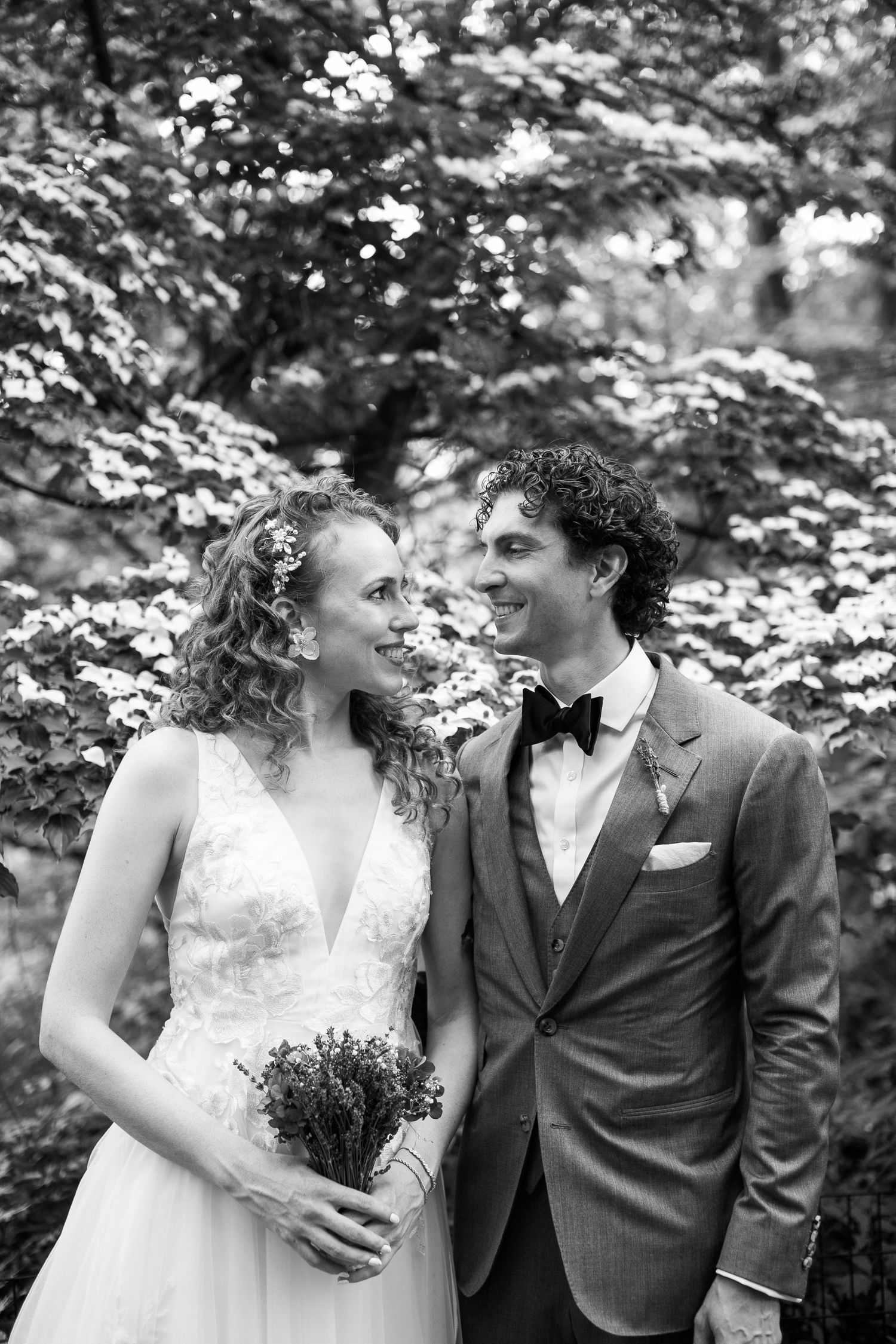 Black and white portrait of smiling bride and groom gazing at each other in a lush garden setting.