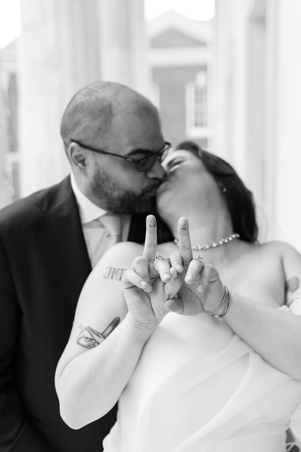 Newlyweds kissing while showing off their wedding rings in a black and white portrait.