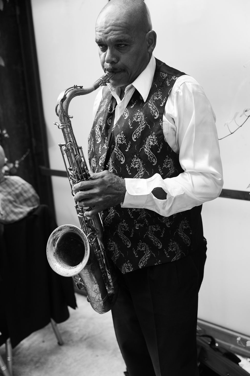 Black and white photo of a jazz musician playing saxophone wearing a patterned vest and white shirt.