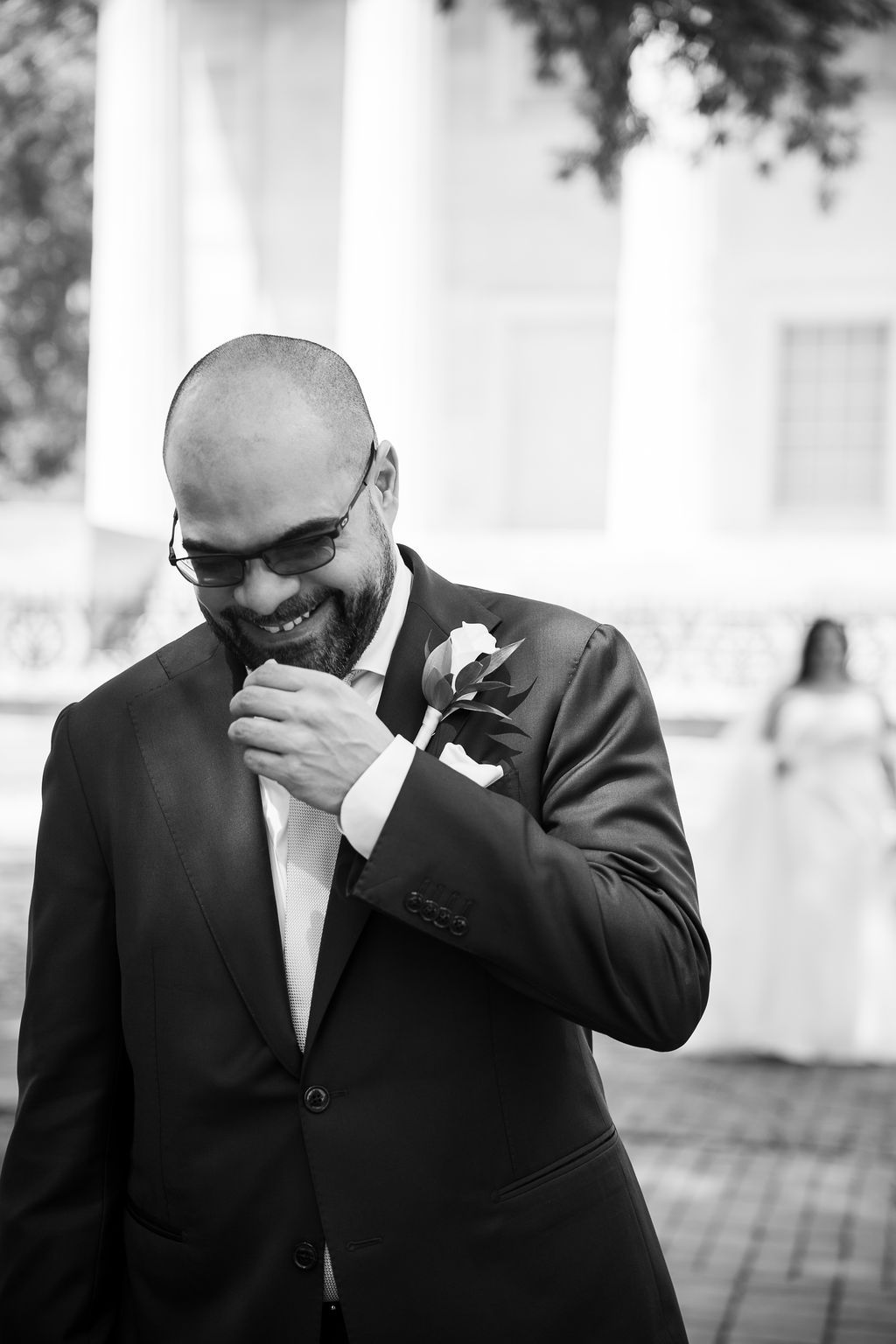 Black and white photo of emotional groom smiling downward during first look at outdoor wedding ceremony.