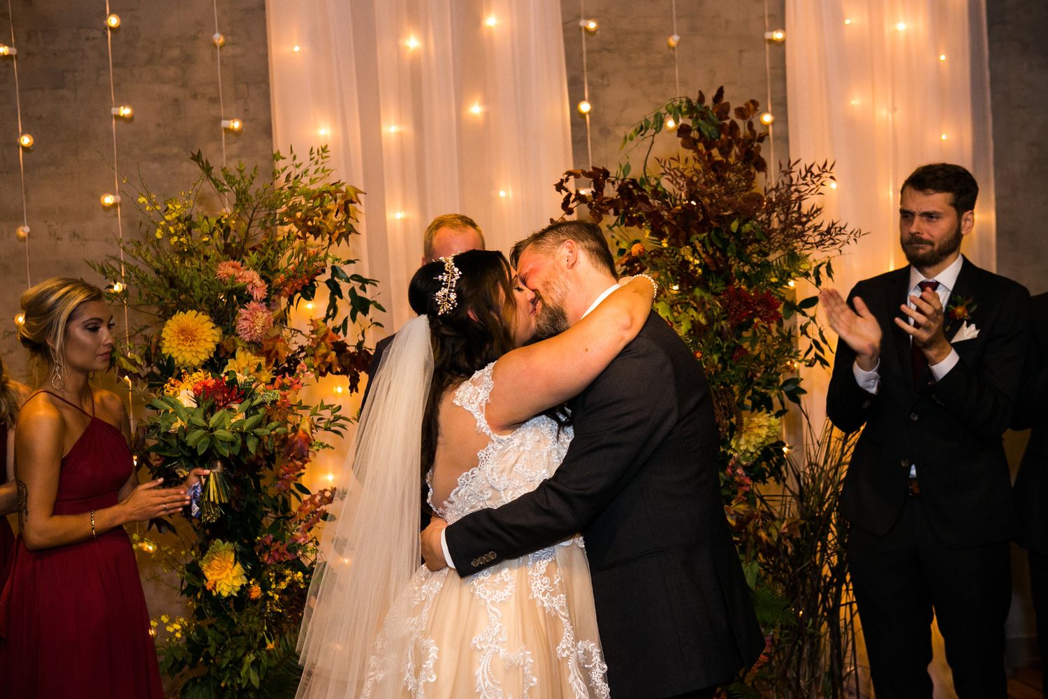 Bride and groom share first kiss surrounded by vibrant fall floral arrangements.