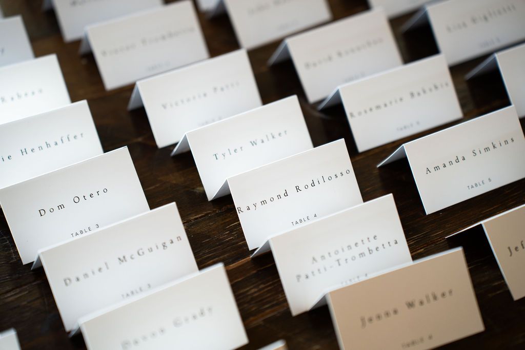 Elegant white wedding place cards arranged on dark wood table for reception seating assignments.