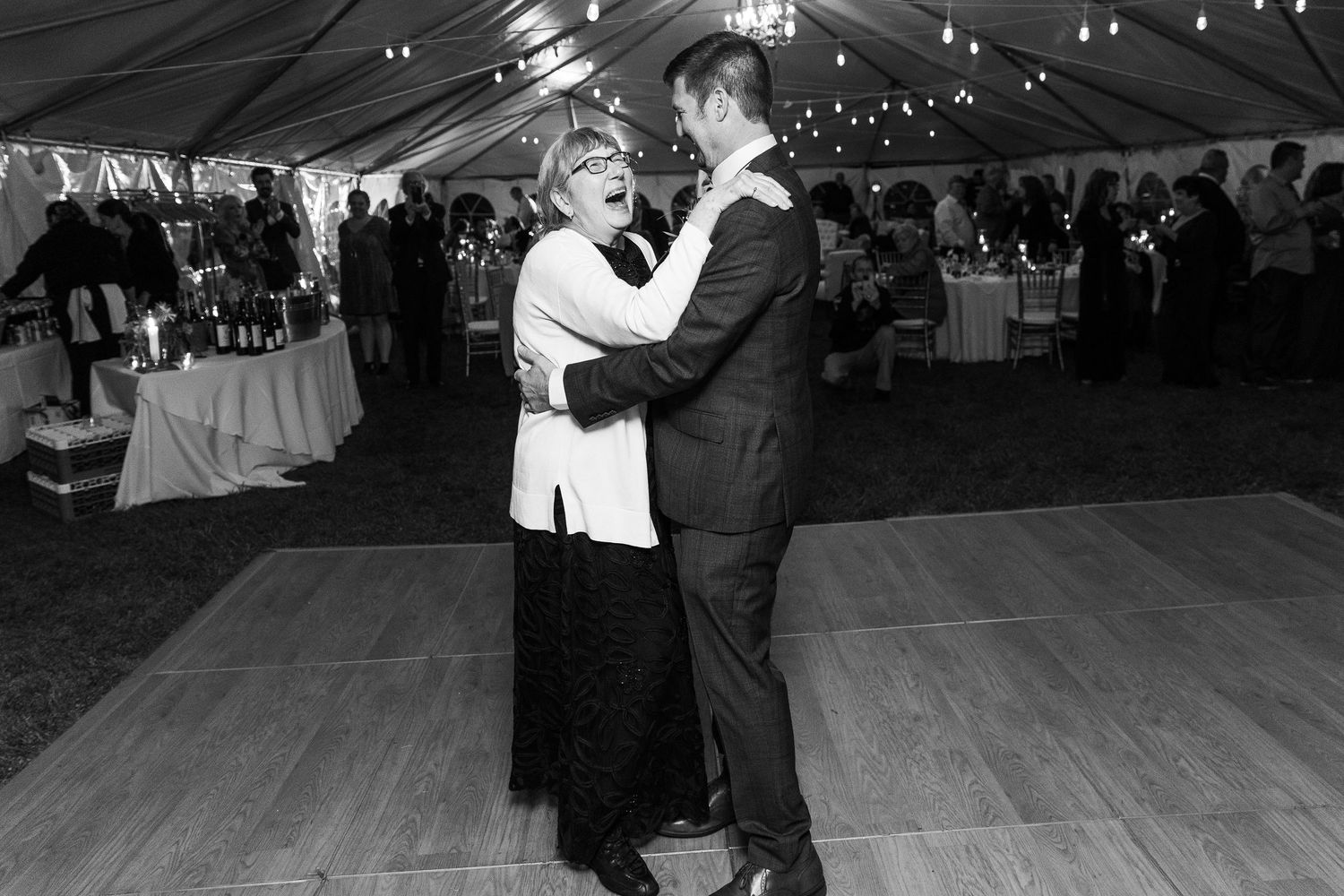 Elderly woman and groom share joyful dance together on wooden floor at wedding reception.