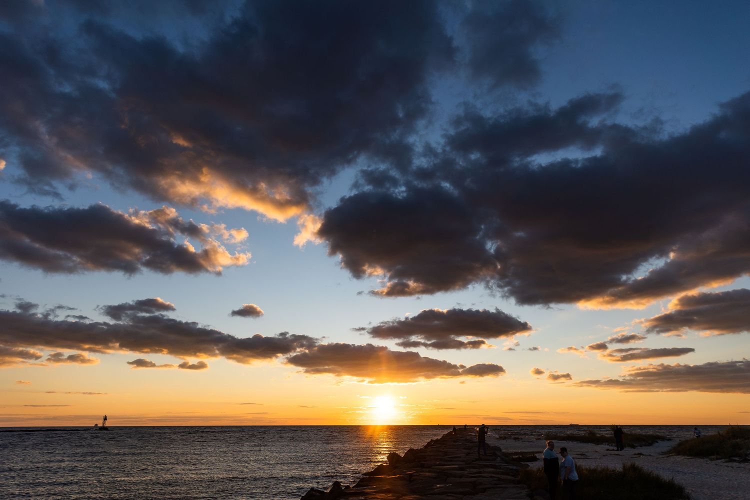 Dramatic golden sunset over calm ocean waters with dark clouds and glowing horizon.