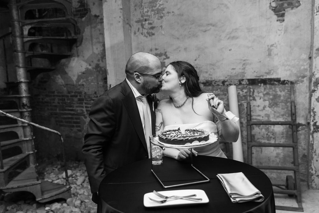 Black and white photo of bride and groom sharing an intimate moment over wedding cake.