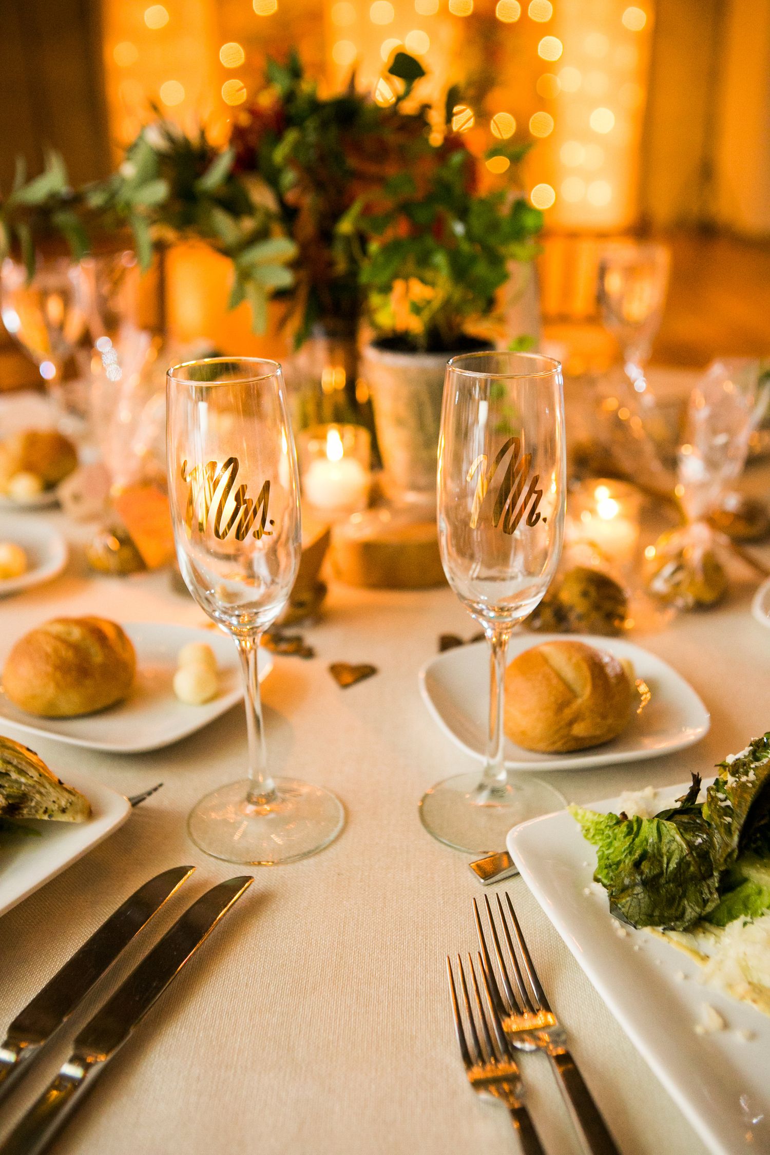 Mr. and Mrs. champagne flutes on a wedding reception table with candles and bread rolls.