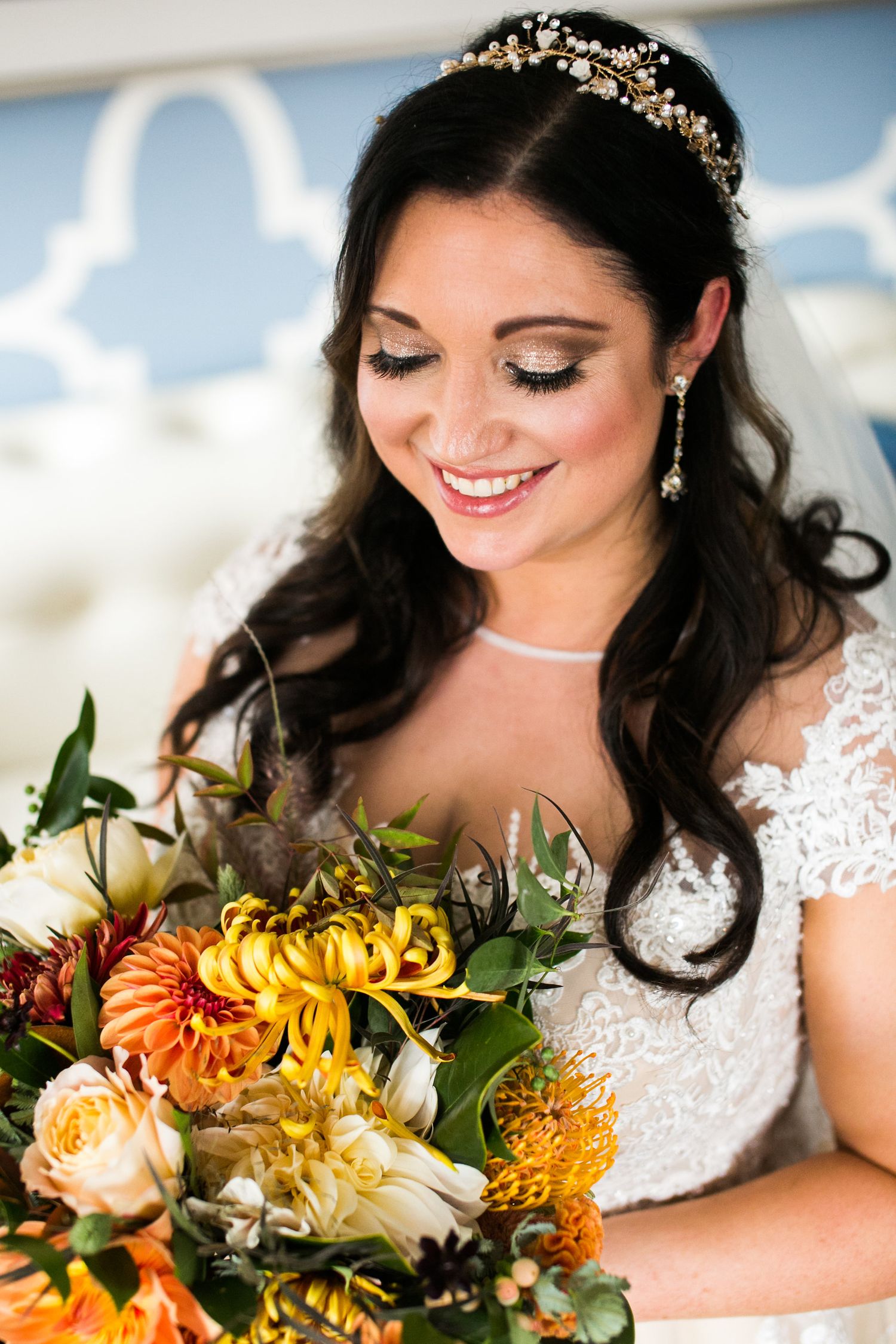 Beautiful dark-haired bride smiling down at colorful autumn wedding bouquet wearing lace gown.