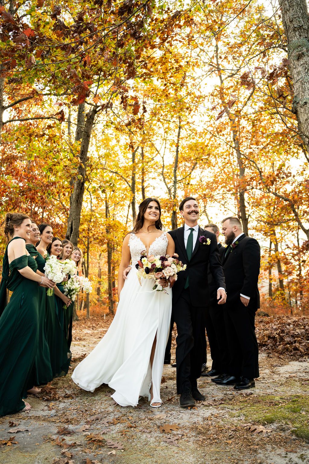 Bride and groom with wedding party in emerald dresses surrounded by vibrant autumn foliage.