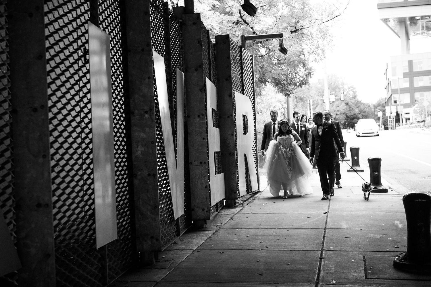 Black and white photo of bride in tulle gown walking along urban sidewalk with groom.