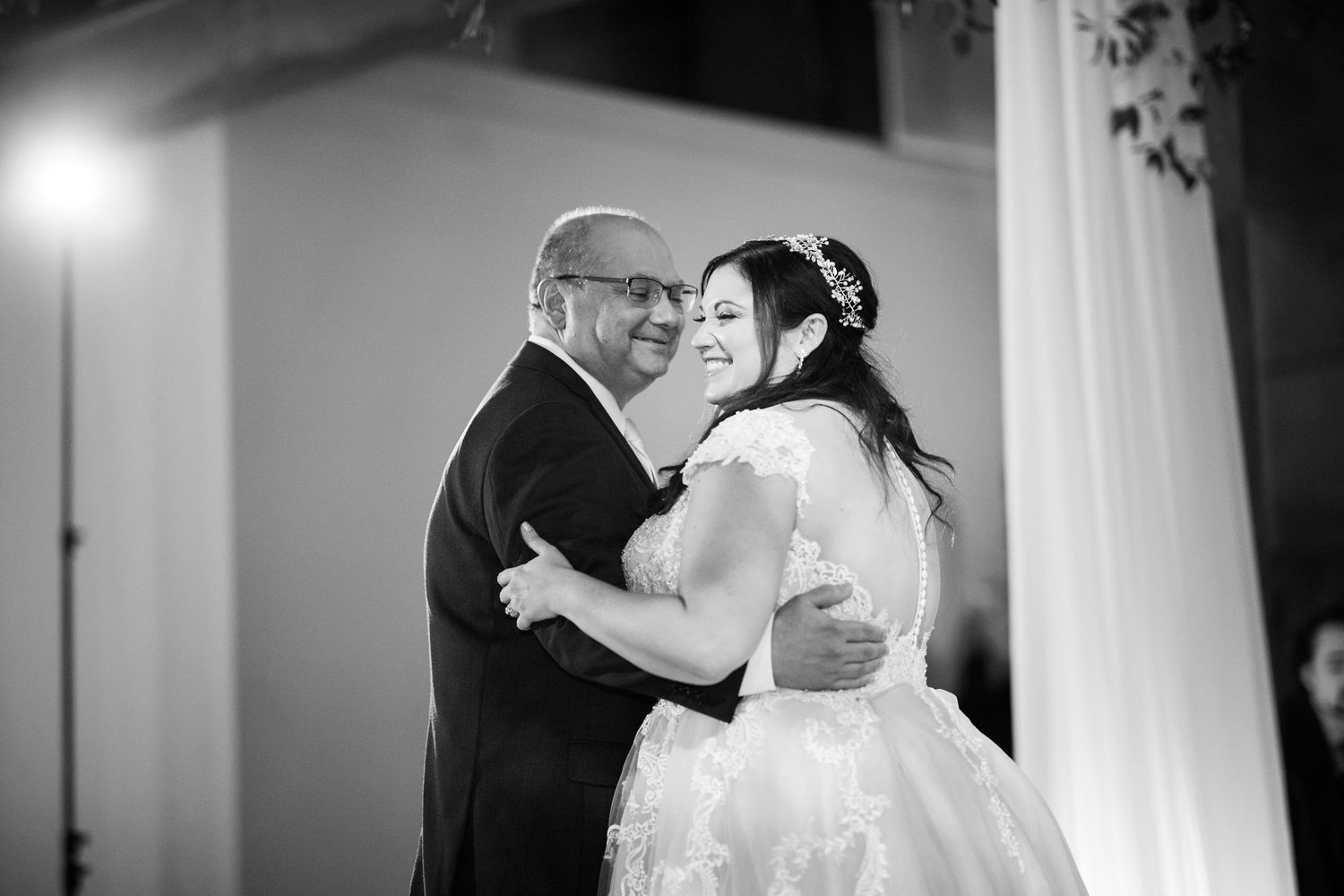 Black and white photo of a smiling bride dancing with her father at a wedding reception.