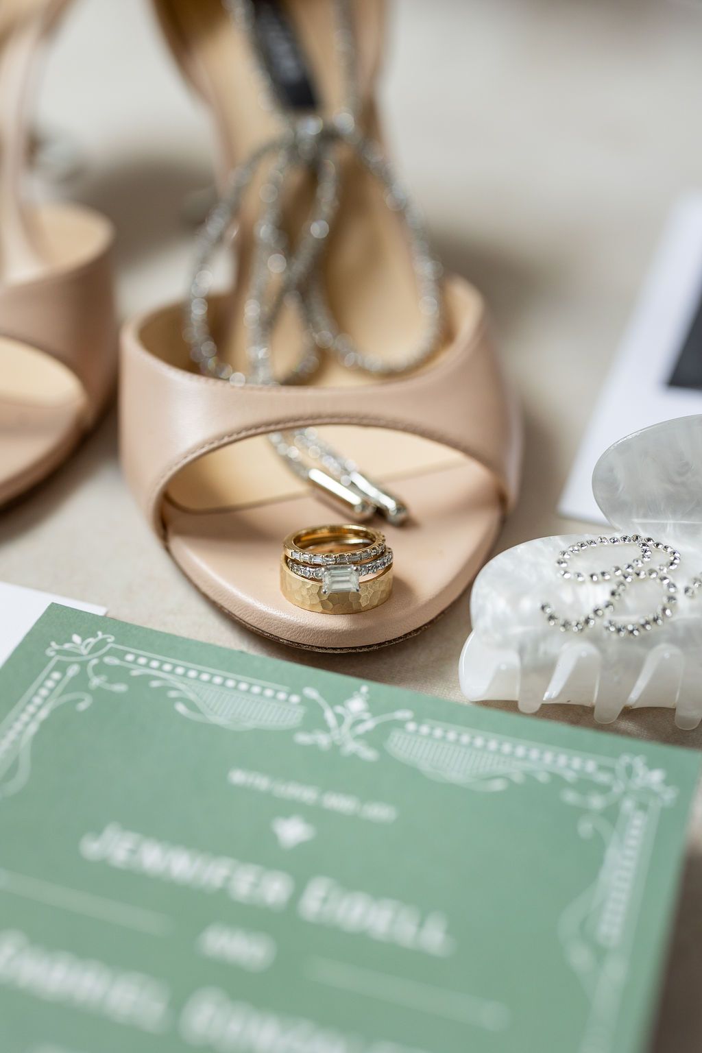 Wedding rings rest inside nude heels beside a green invitation for Jennifer Eidell and Gabriel Gonzalez.