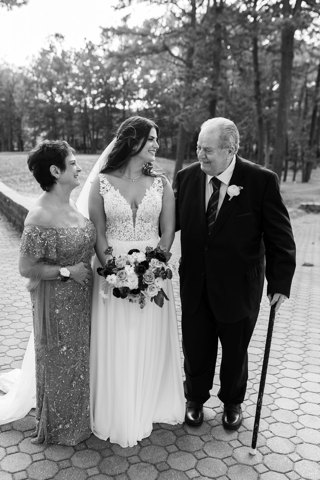 Bride with parents on wedding day, black and white photo, father using cane, mother in sequined gown, outdoor setting.