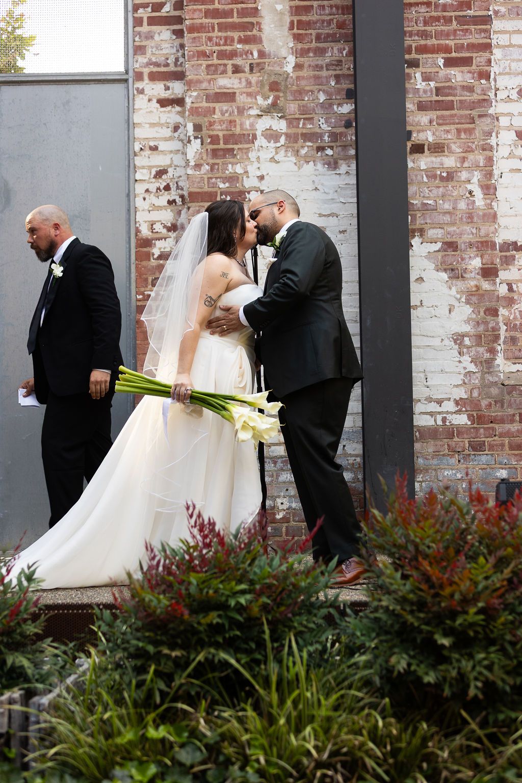 Bride and groom share a kiss outside a rustic brick wall wedding venue.