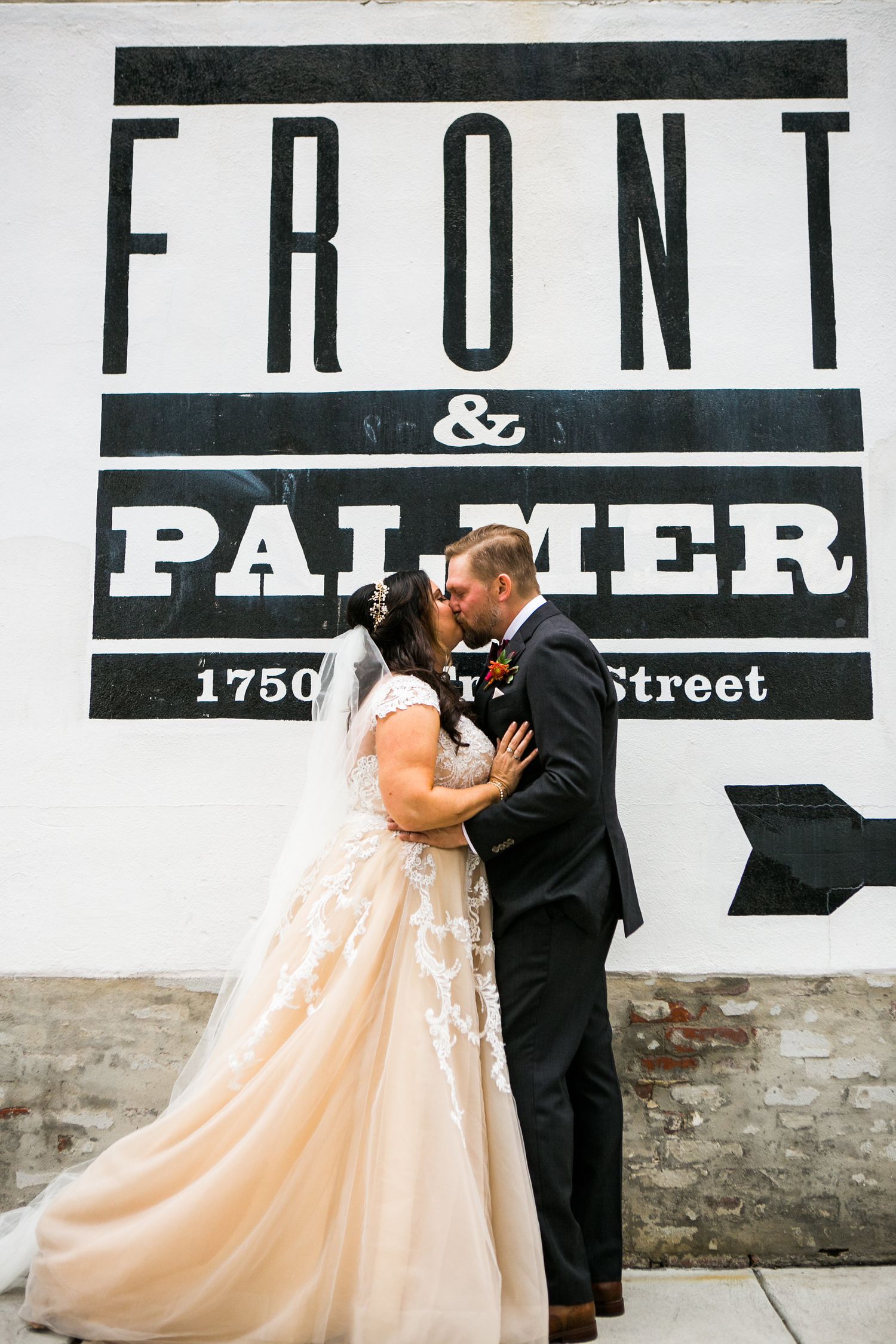 Bride and groom share a kiss in front of the Front and Palmer wedding venue brick wall sign.