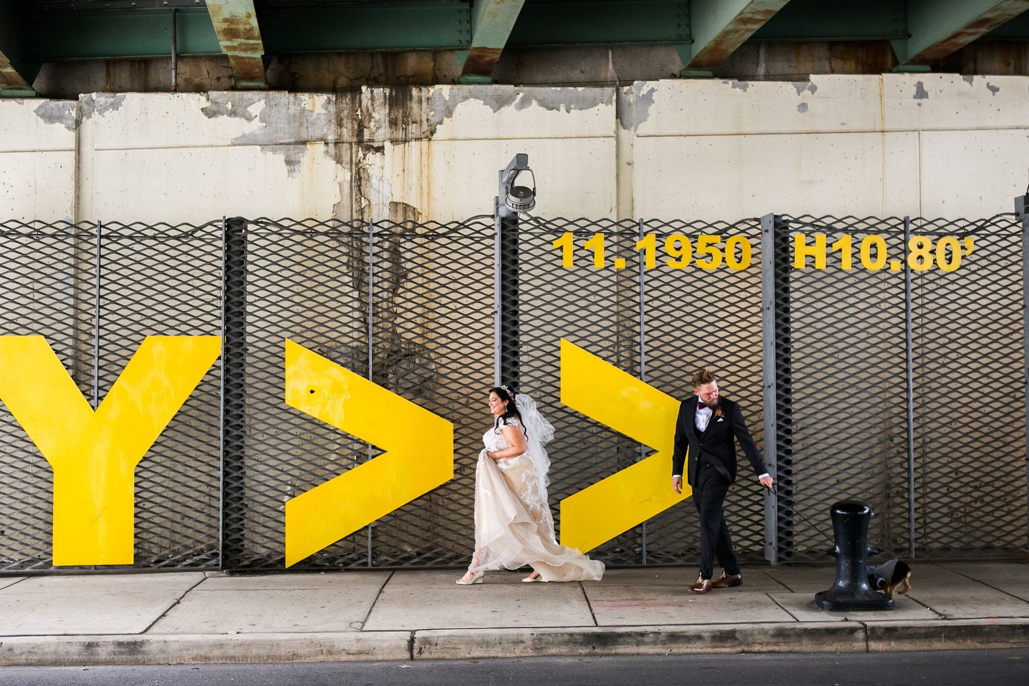 Bride and groom walk past a bold yellow graphic mural on a city street on their wedding day.