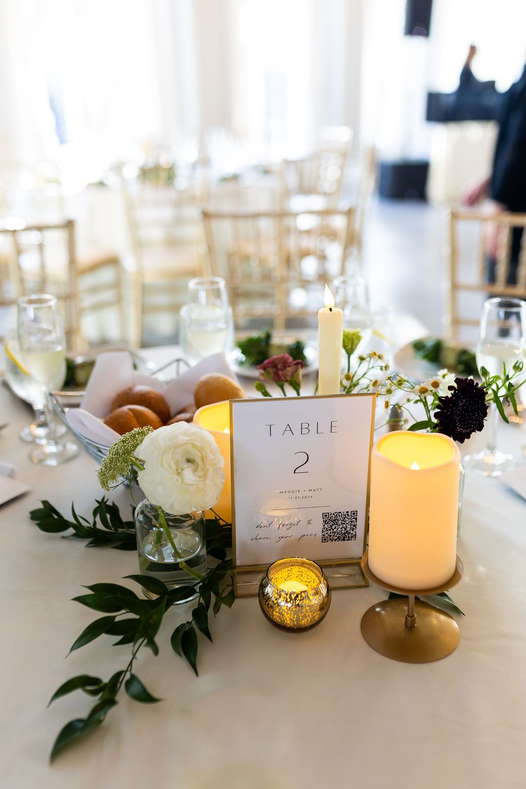 Wedding reception Table 2 centerpiece with white candles, greenery, white flowers, and gold accents.